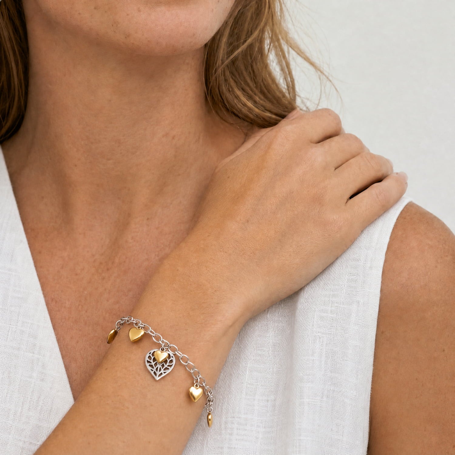 Model wears a sterling silver chain bracelet featuring a sculptural cut-out heart charm with yellow gold vermeil accents.
