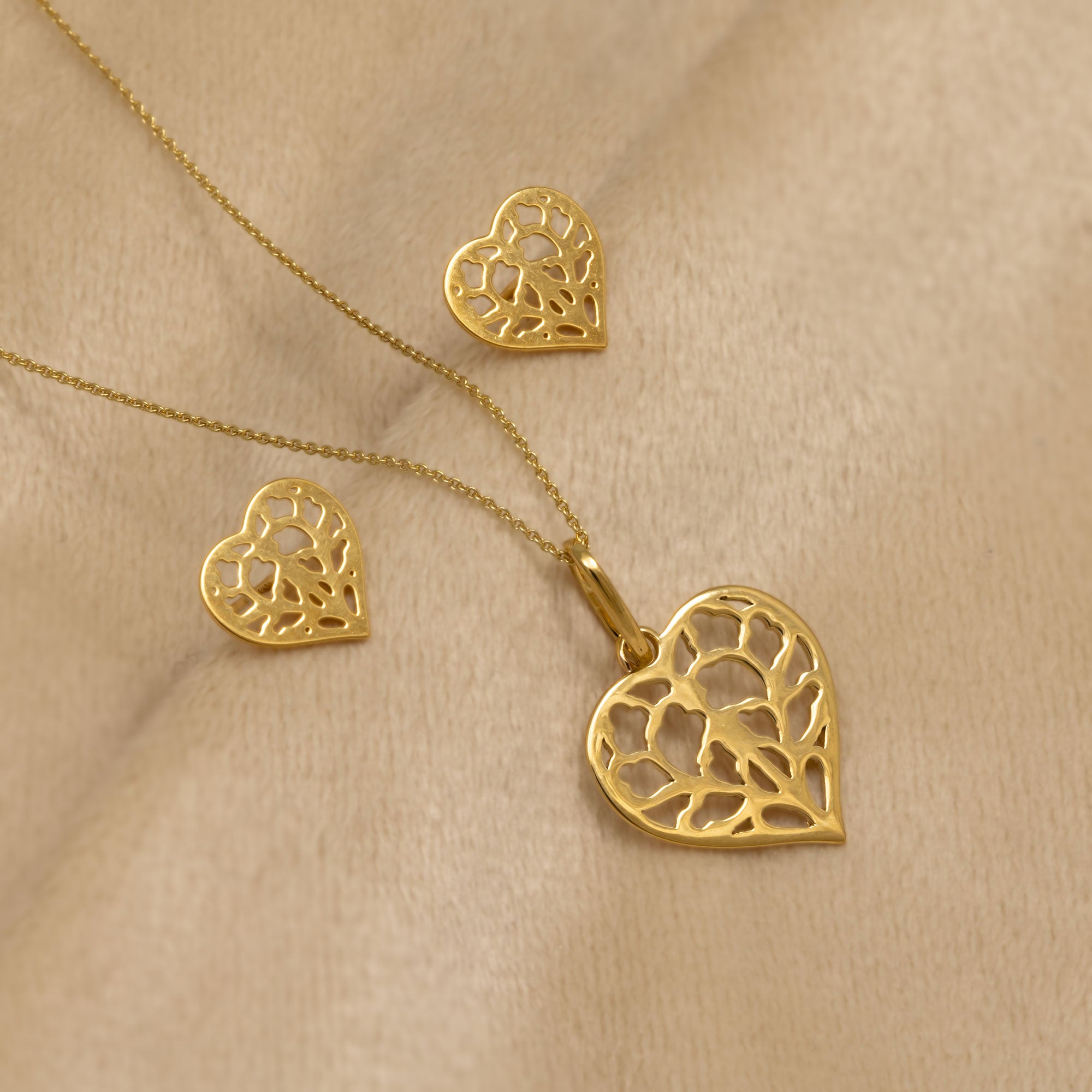 9 carat yellow gold heart-shaped pendant and matching stud earrings featuring an openwork design inspired by York Minster with a delicate, sculptural finish placed on a cream velvet cloth.