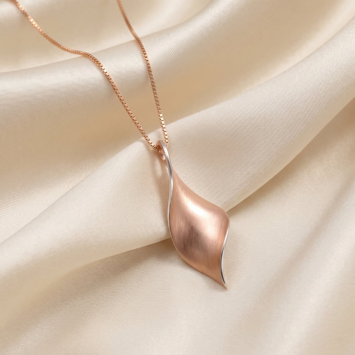 A rose gold vermeil twist pendant on a cream satin background