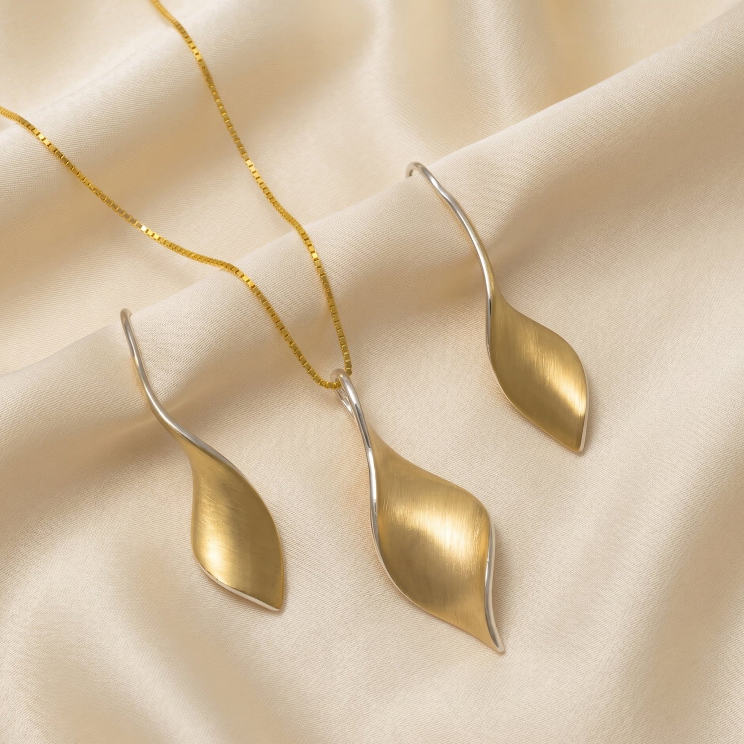 Yellow gold vermeil twisting pendant and earring set on a cream silk background