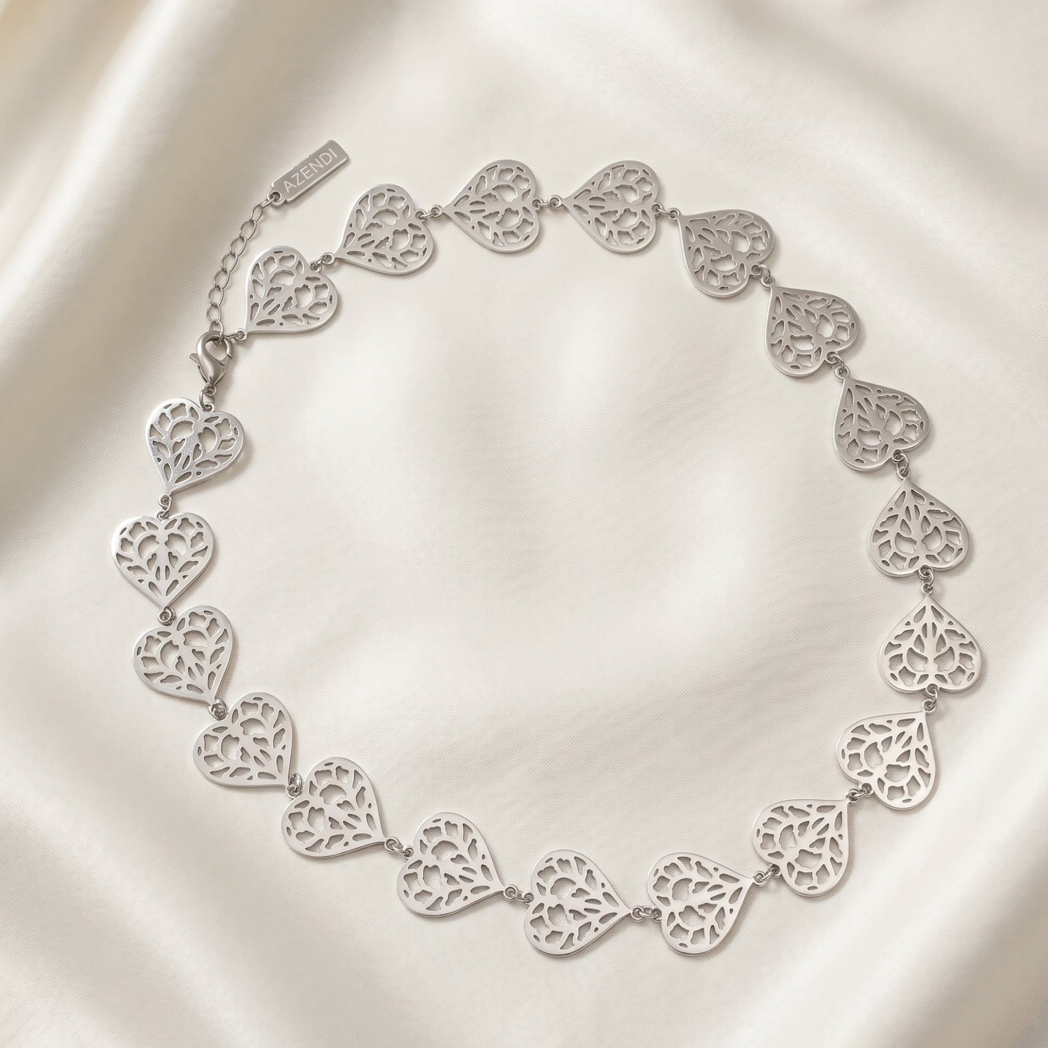 Sterling silver necklace featuring a series of sculptural openwork heart links with intricate filigree detail, designed with an adjustable chain for versatile length laid on a white silk background.