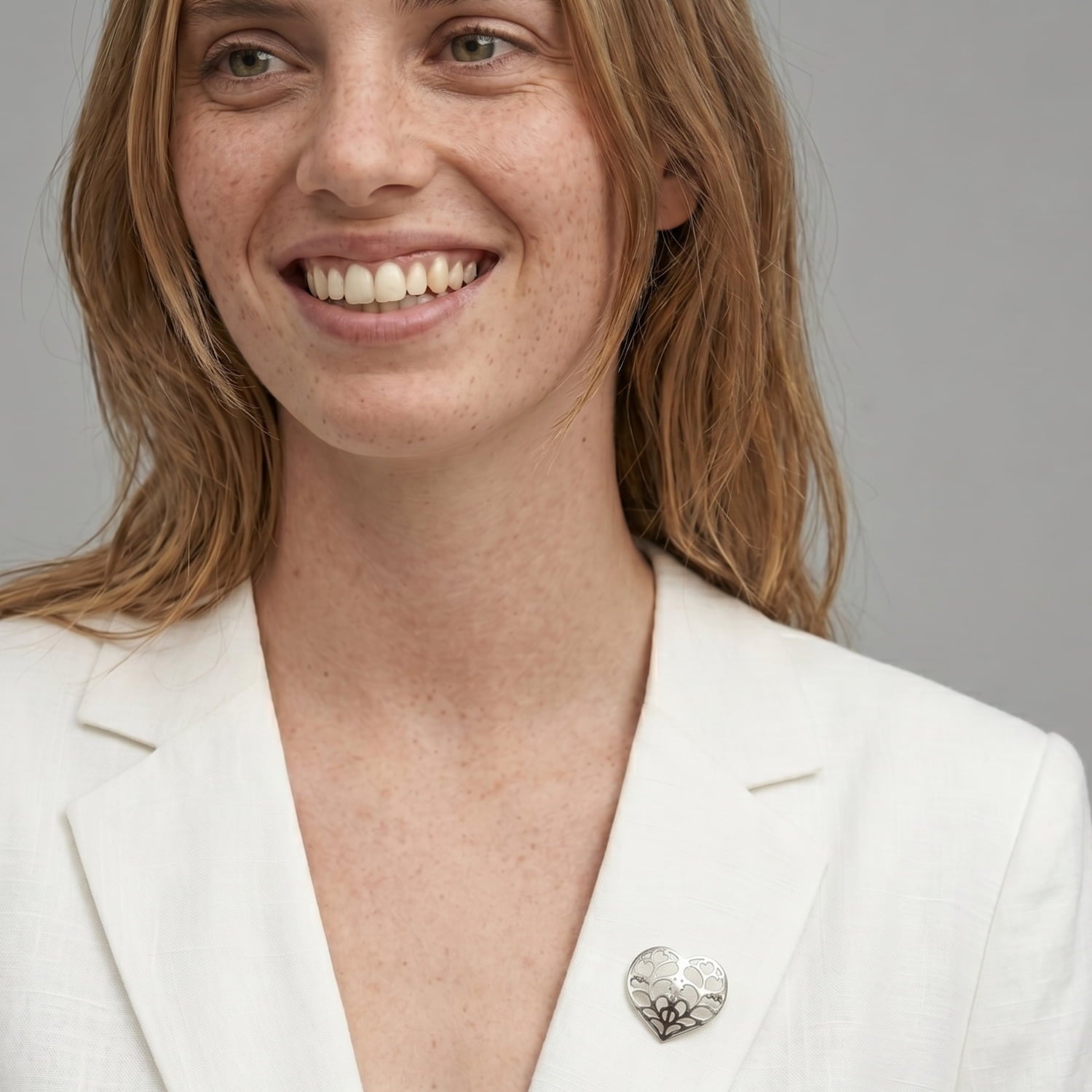 Sterling silver heart-shaped brooch with intricate openwork design, styled on a white blazer lapel, showcasing contemporary British silver jewellery craftsmanship.