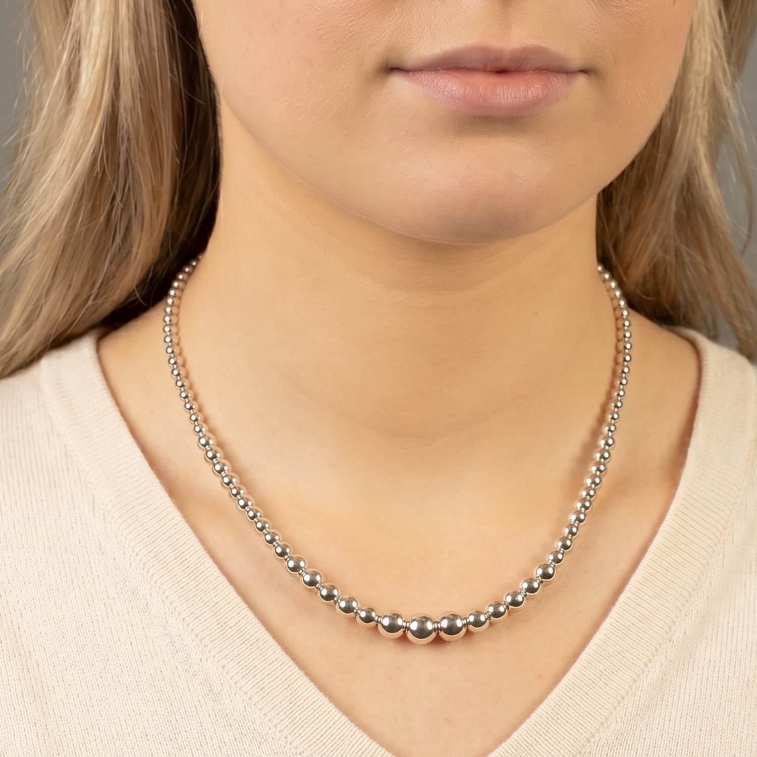 Close-up of a person wearing a silver beaded necklace against a neutral background