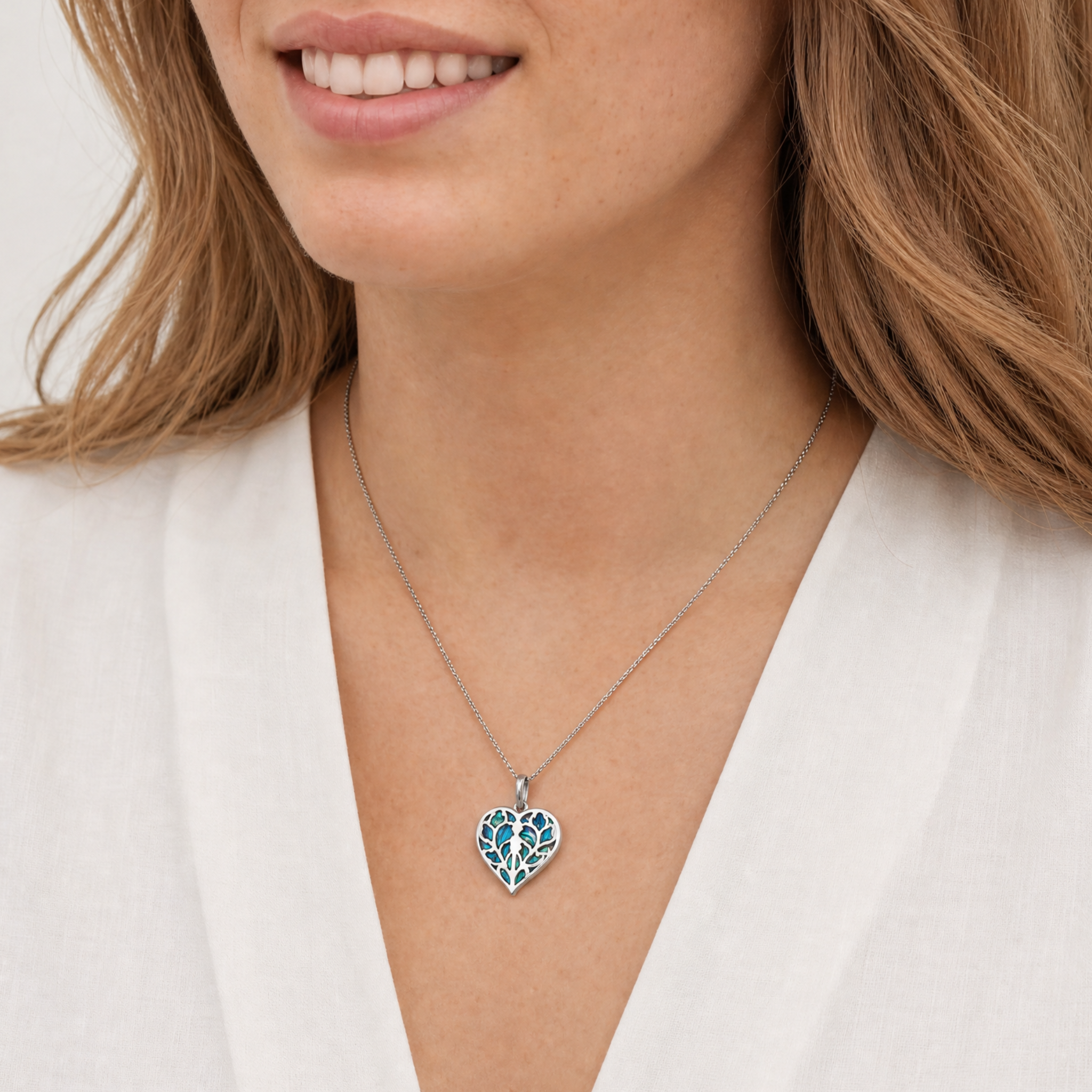 Model wears sterling silver pendant featuring an openwork heart design with iridescent abalone inlay, suspended from a delicate fine silver chain.