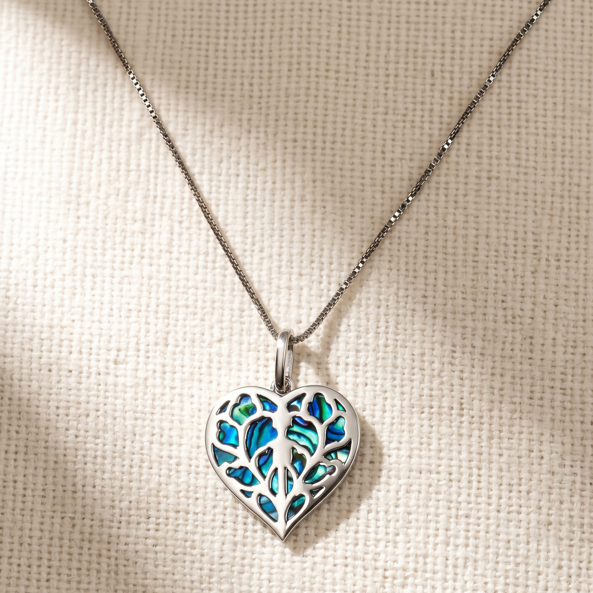 Sterling silver pendant featuring an openwork heart design with iridescent abalone inlay, suspended from a delicate fine silver chain.