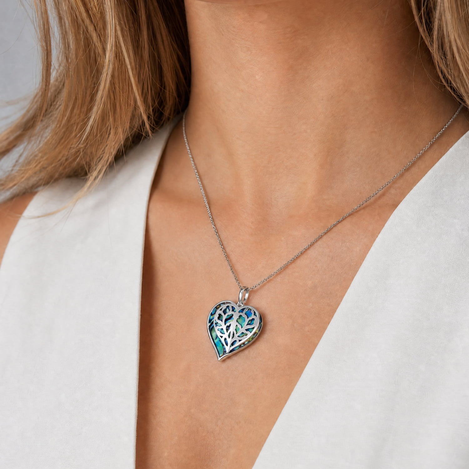 Sterling silver double heart pendant featuring an intricate abalone inlay, suspended from a fine chain, styled with a crisp white waistcoat.