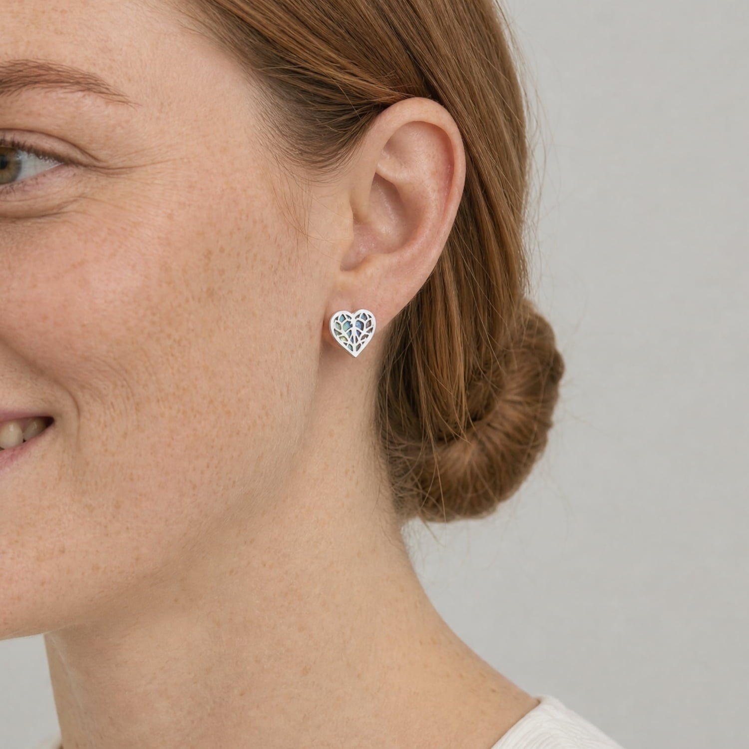 Sterling silver heart-shaped stud earring with intricate cut-out abalone-inspired design, worn on the earlobe, showcasing fine British craftsmanship.