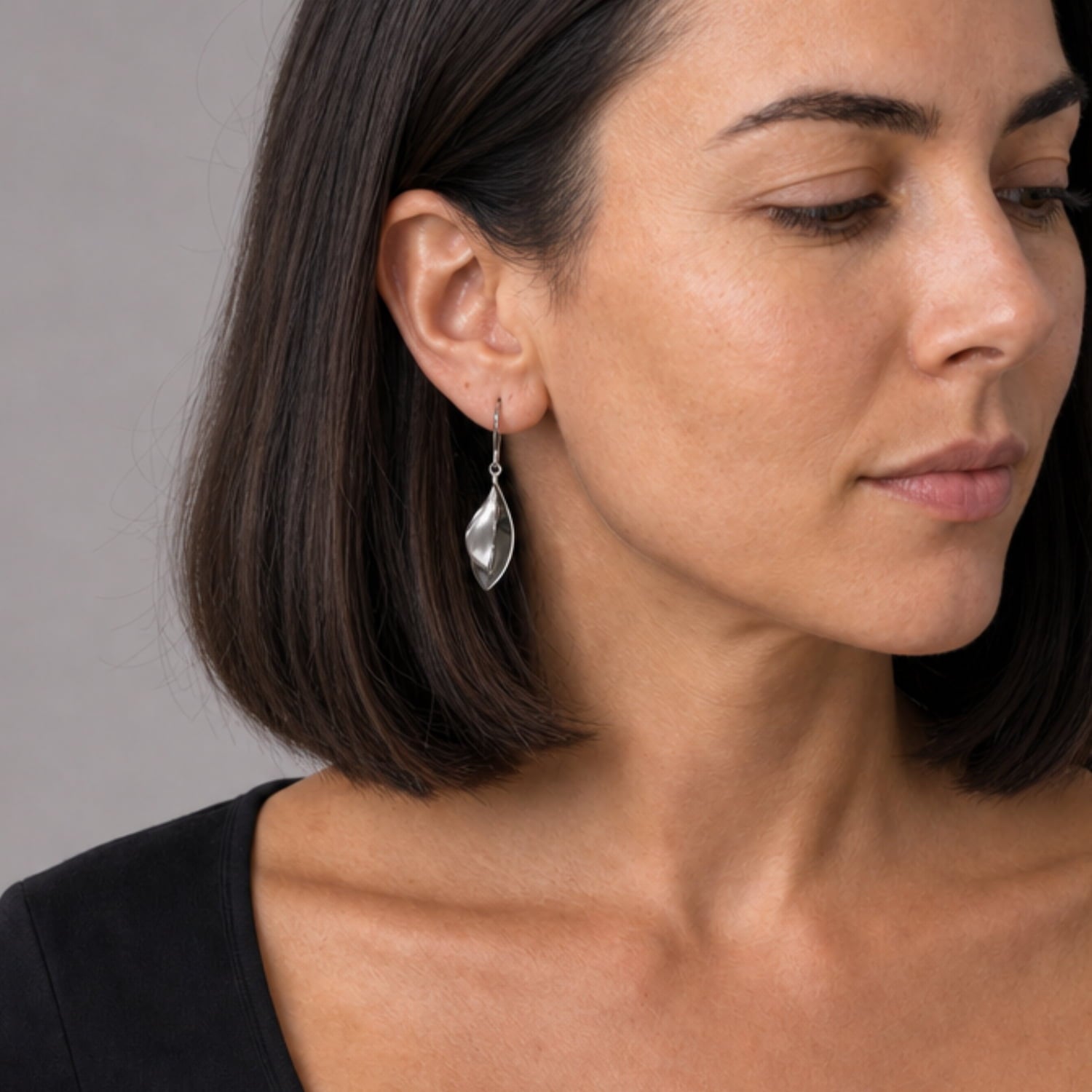 Model wears sterling silver drop earrings shaped as double leaves, featuring smooth, polished surfaces and a graceful, sculptural design for refined contemporary silver jewellery.
