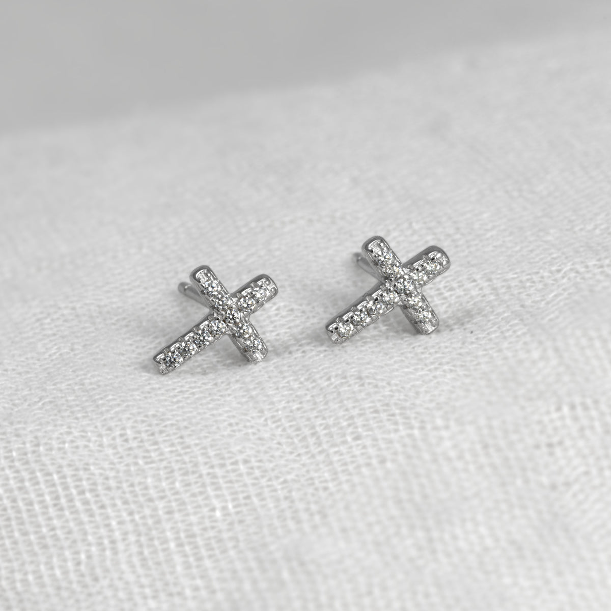 Delicate sterling silver stud earrings shaped as crosses, each adorned with pavé-set stones for a subtle, refined sparkle on a white background.