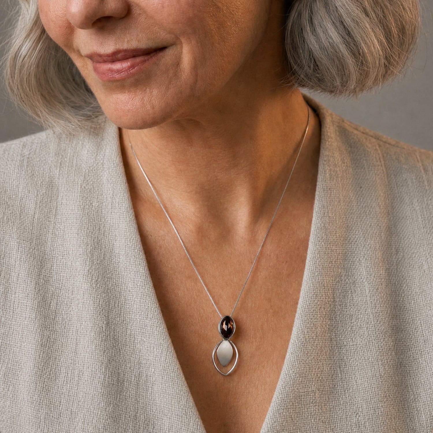 A close-up of a woman wearing sterlign silver pendant with a dark amber stone, paired with a light beige linen top.
