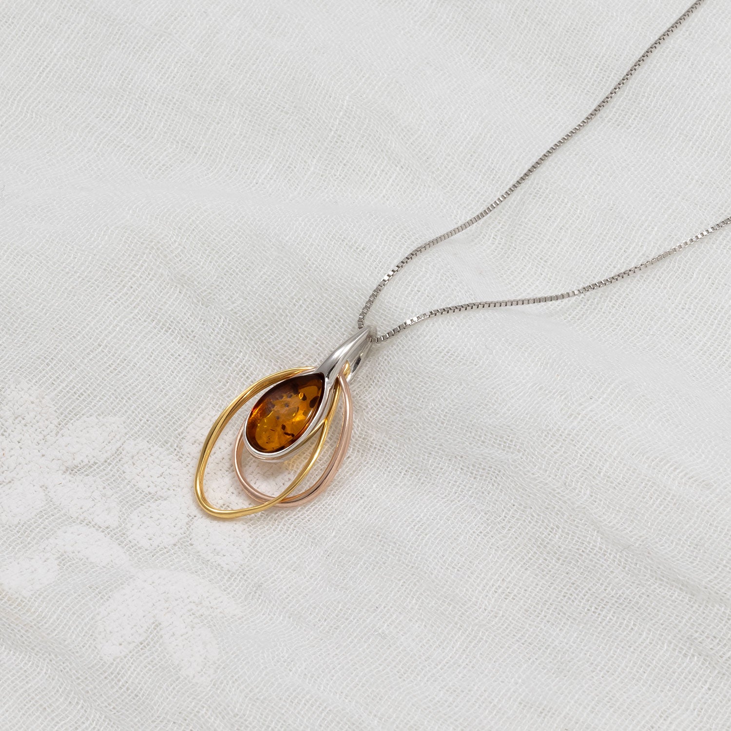 Sterling silver pendant featuring a teardrop amber gemstone framed by layered yellow and rose gold vermeil loops, suspended from a fine silver chain with a contemporary sculptural design.