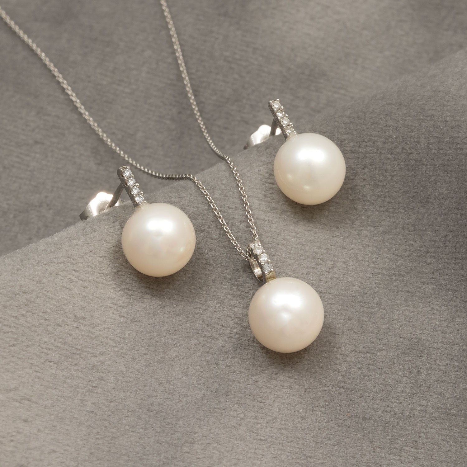 Elegant 9ct white gold stud earrings with lustrous pearls and a row of sparkling diamonds, paired with a matching pearl pendant necklace showcasing refined contemporary design.