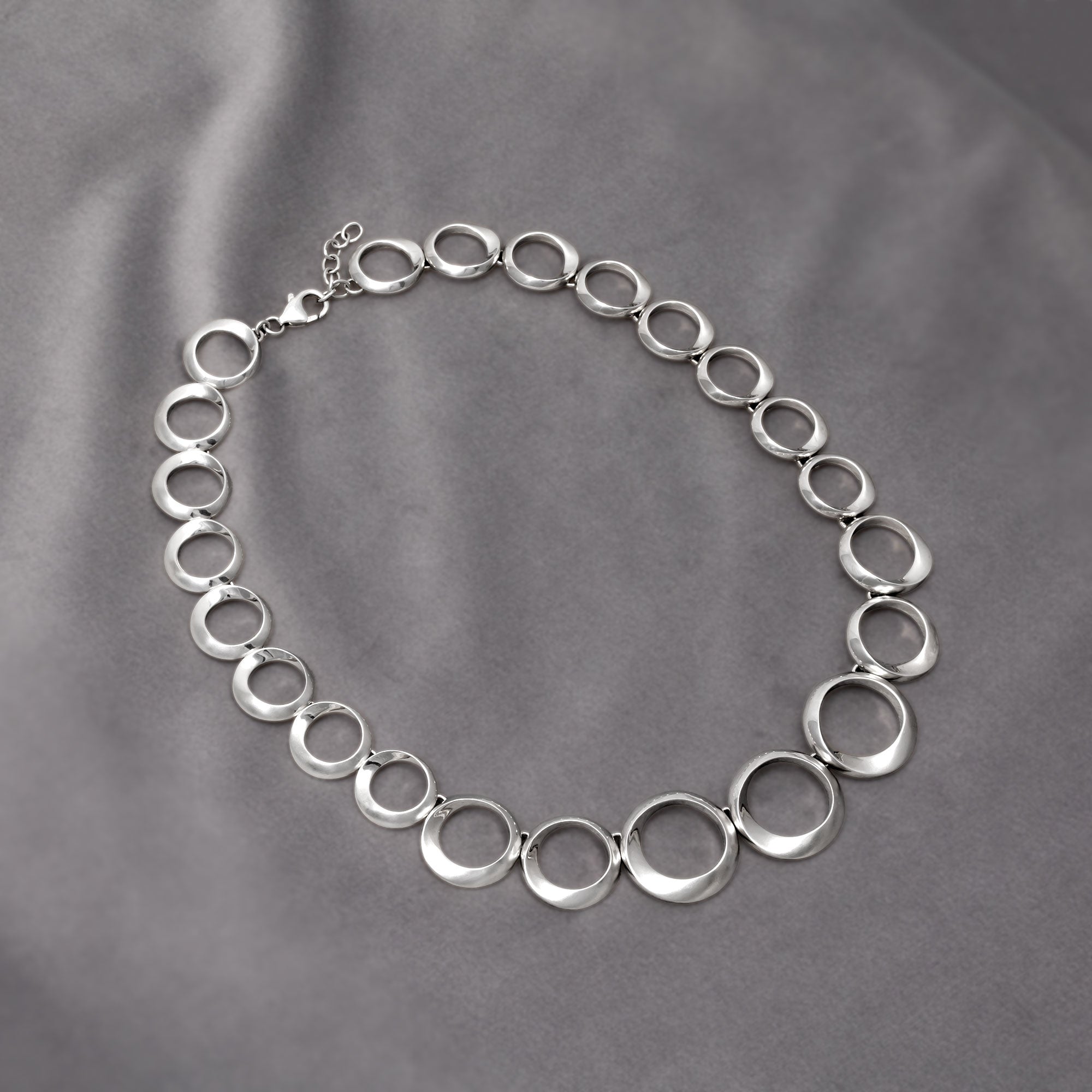 Necklace featuring graduated circle links with alternating satin and polished finishes in sterling silver, presenting a modern, sculptural design for refined silver jewellery. Placed on a grey velvet cloth.