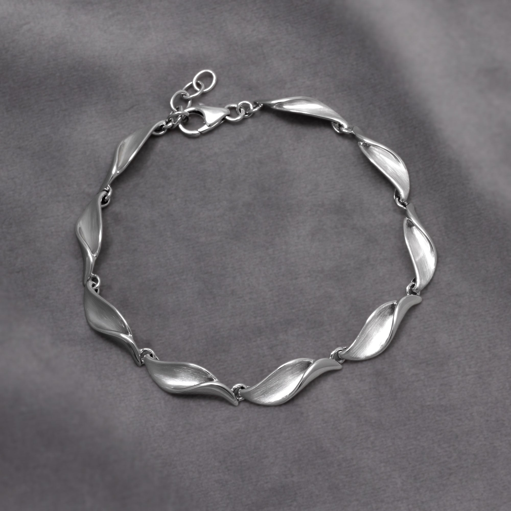 Delicate sterling silver bracelet featuring a series of folded wave-shaped links with a satin and polished finish, designed for refined contemporary silver jewellery. Placed on a grey velvet cloth.