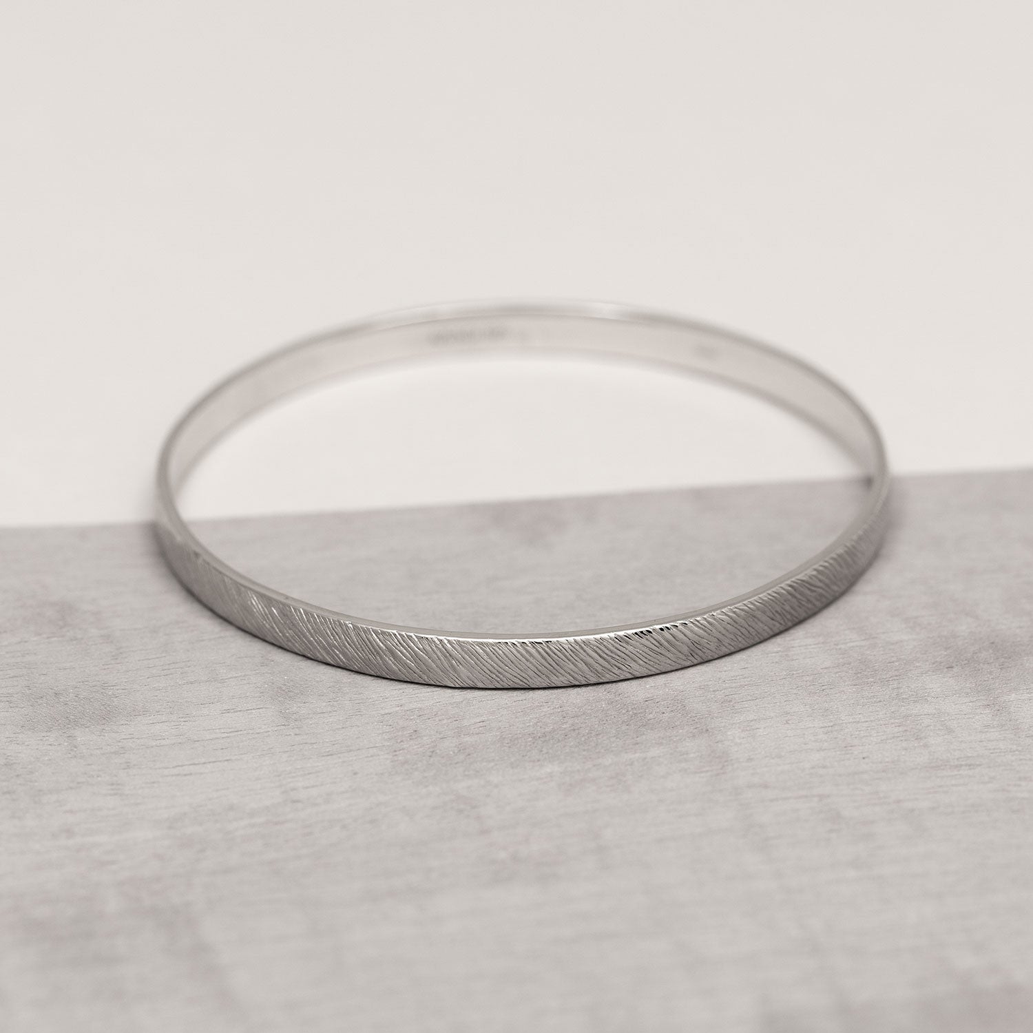 Sterling silver bangle featuring a subtle diagonal textured pattern on a slim band, embodying a modern and refined design by Azendi.