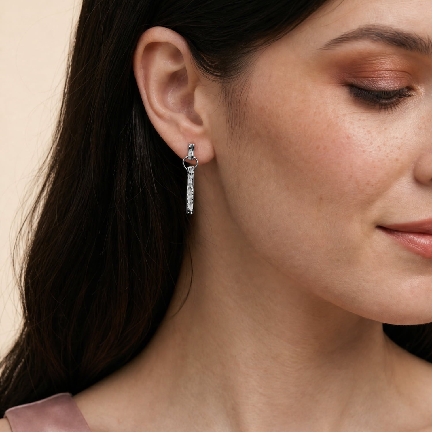 A close-up of a woman wearing textured sterling silver drop earrings
