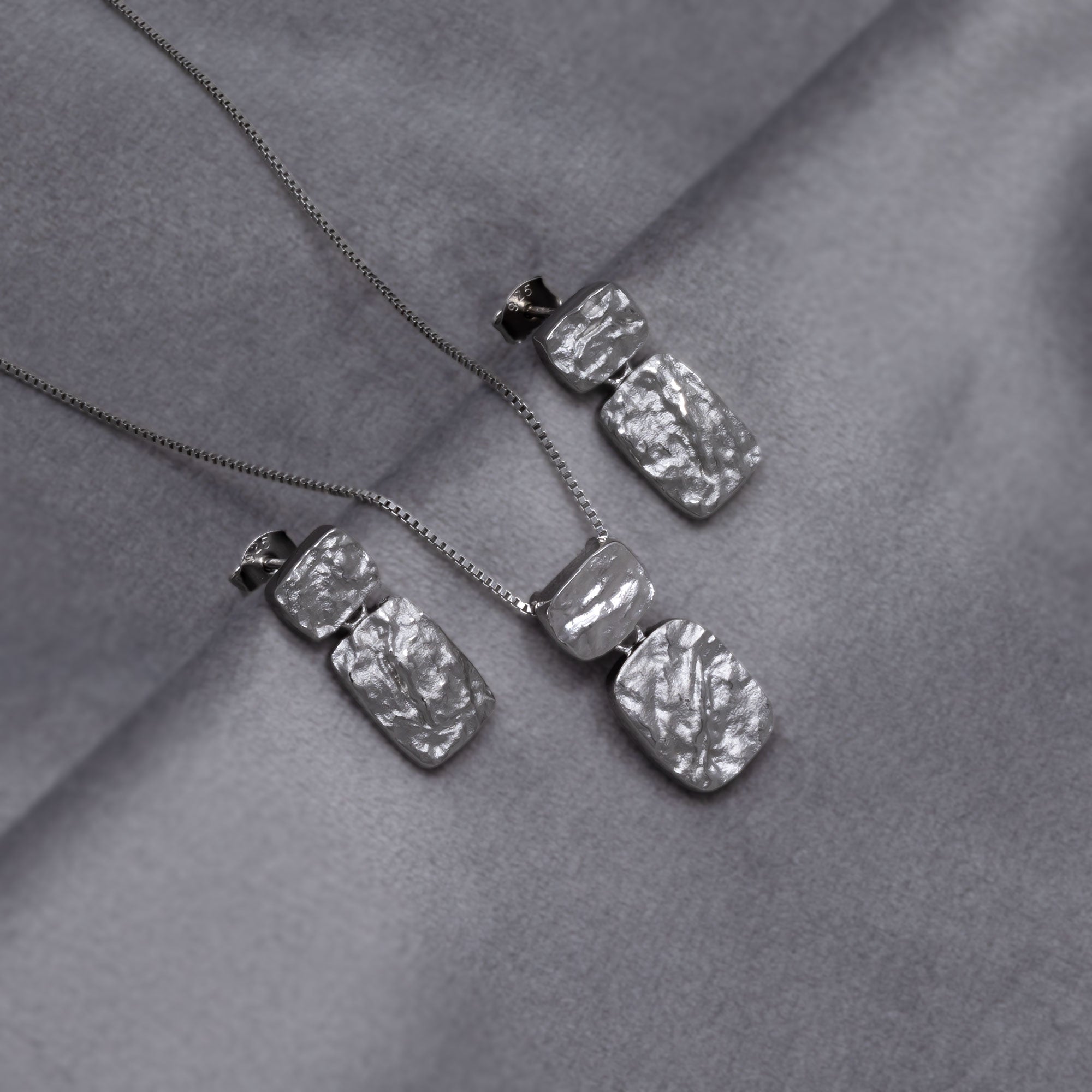 Rectangular pendant and drop earrings in polished sterling silver featuring an organic, textured surface with a modern sculptural design for refined British silver jewellery.