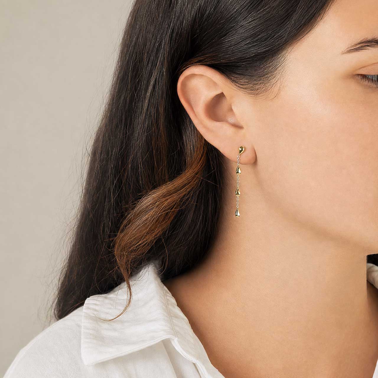 Close-up of a model wearing silver and gold vermeil droplet earrings with a neutral background
