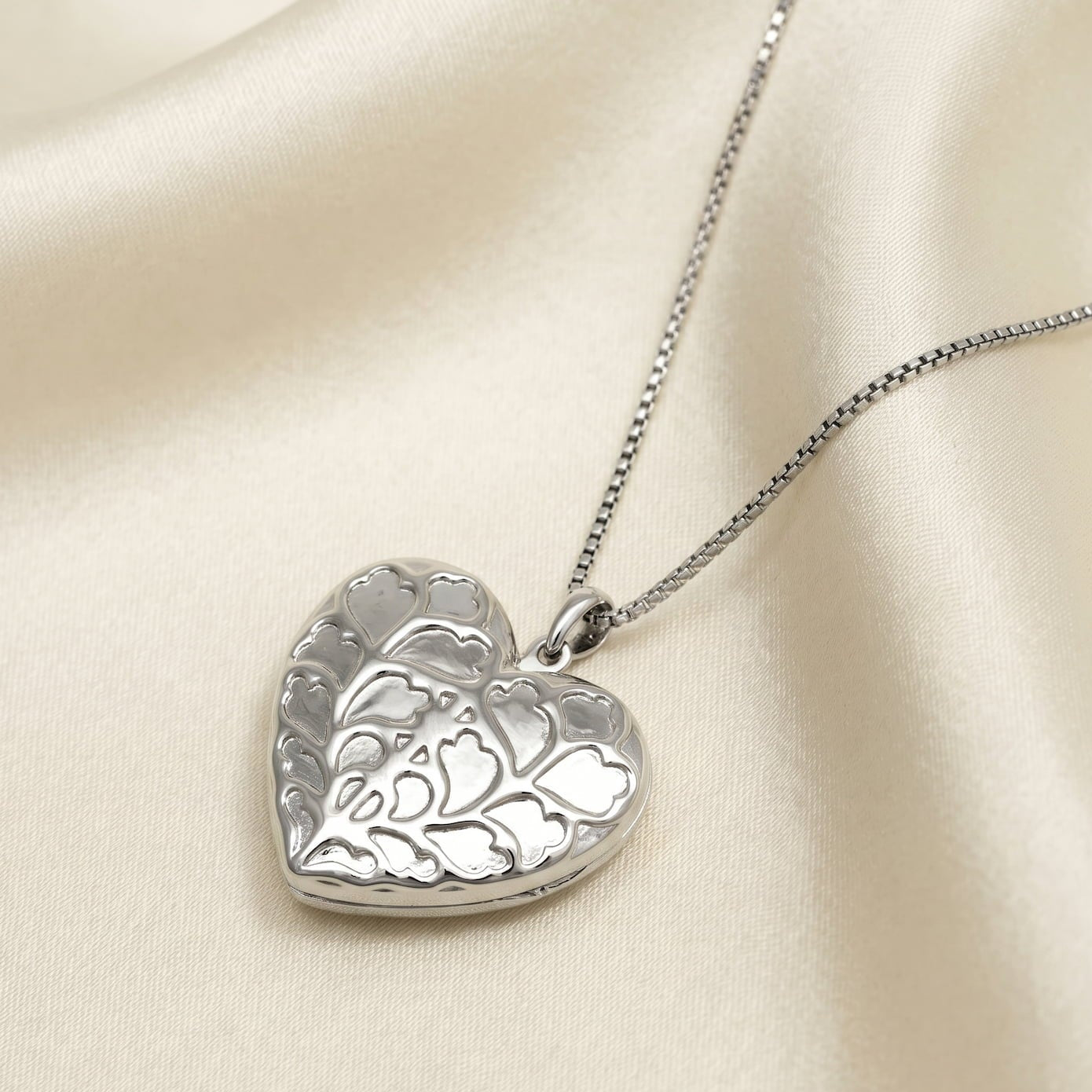 Sterling silver heart-shaped locket pendant with a sculptural textured surface, suspended on a delicate chain, showcasing expert British craftsmanship and elegant design.