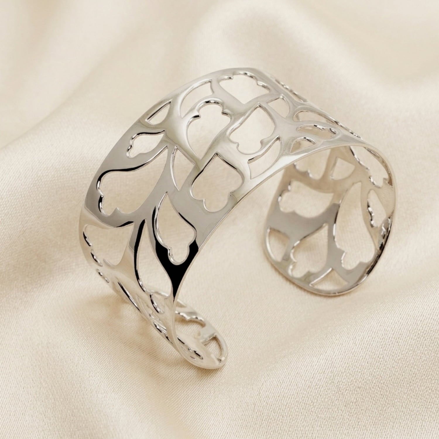 Openwork sterling silver cuff bangle featuring detailed heart-inspired motifs, resting on soft neutral fabric, showcasing refined British craftsmanship.