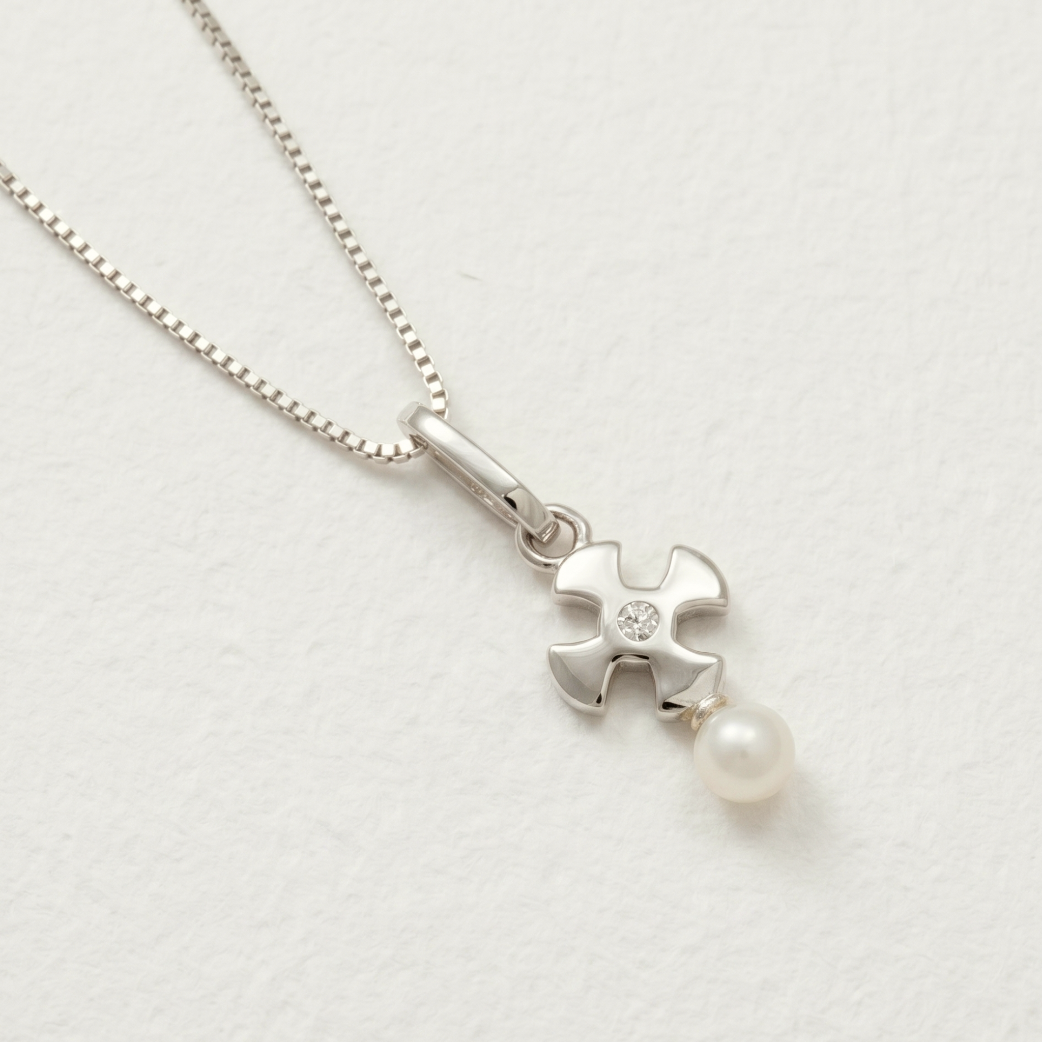Sterling silver pendant featuring a sculptural St Cuthbert cross design with a central clear stone and a single freshwater pearl drop, displayed on a white background.