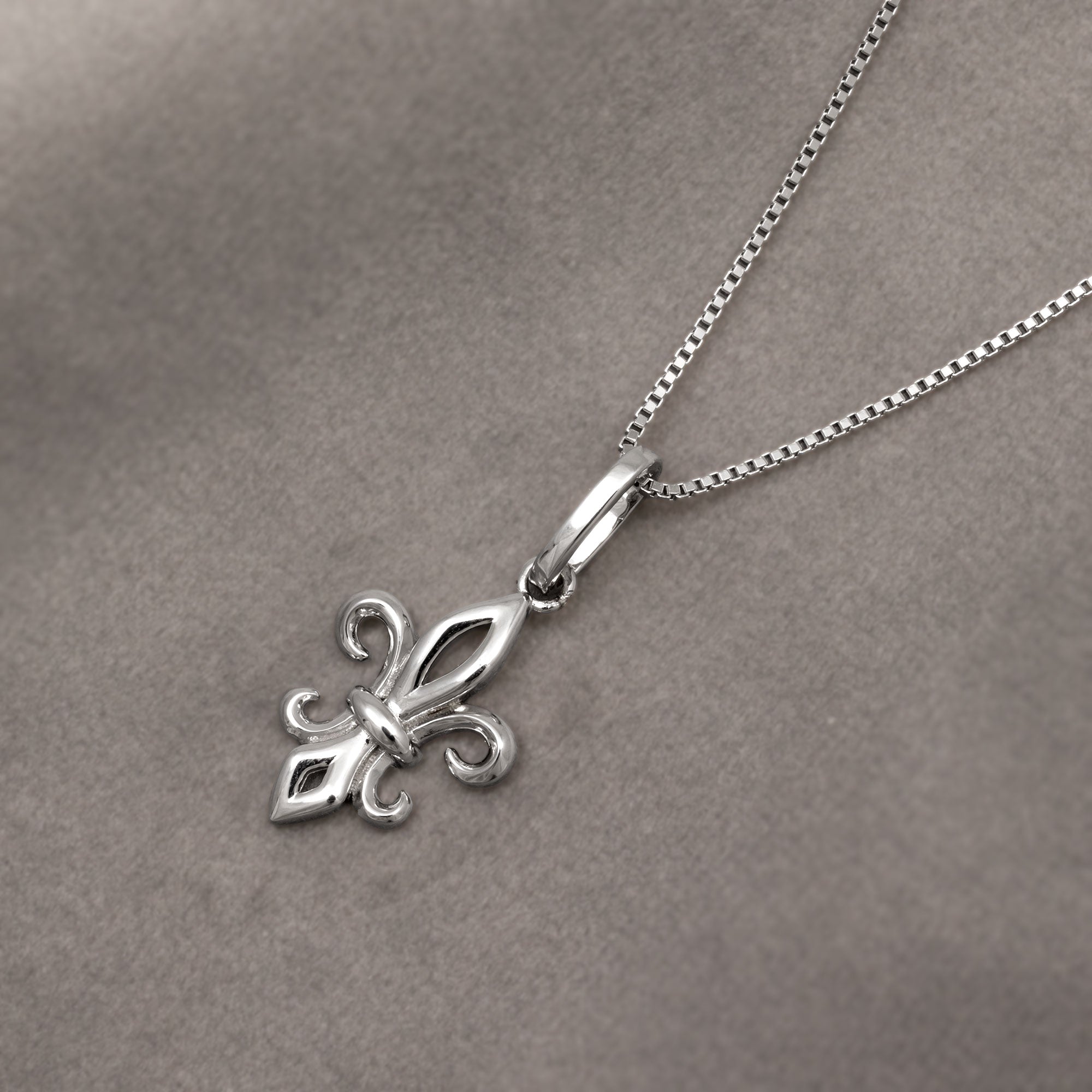 Sterling silver pendant featuring a sculptural fleur de lis design suspended from a delicate silver chain, embodying timeless elegance and expert craftsmanship. Placed on grey velvet cloth.