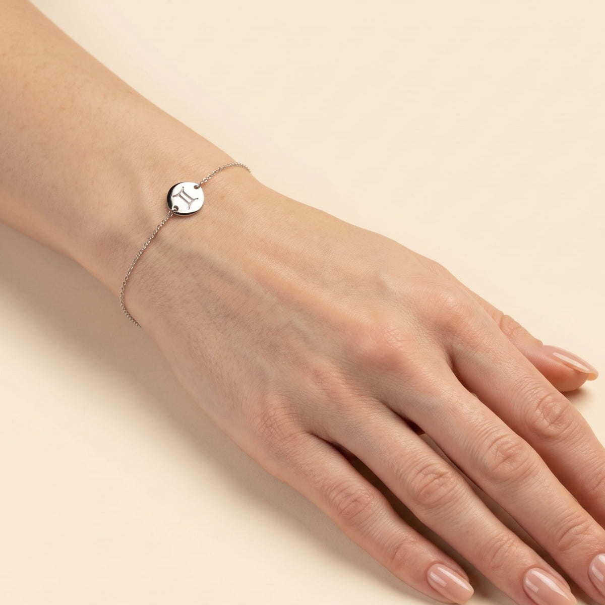 Delicate sterling silver bracelet featuring an adjustable sliding bead and a polished charm engraved with the Gemini zodiac symbol, worn on the wrist.