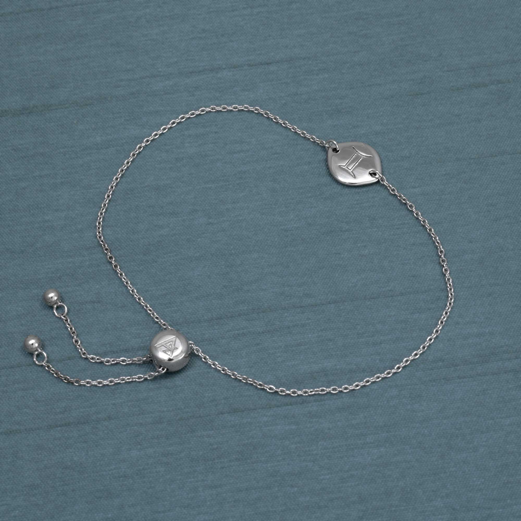Delicate sterling silver adjustable bracelet featuring a circular zodiac charm engraved with the Gemini symbol, finished with a sliding bead for customizable fit.