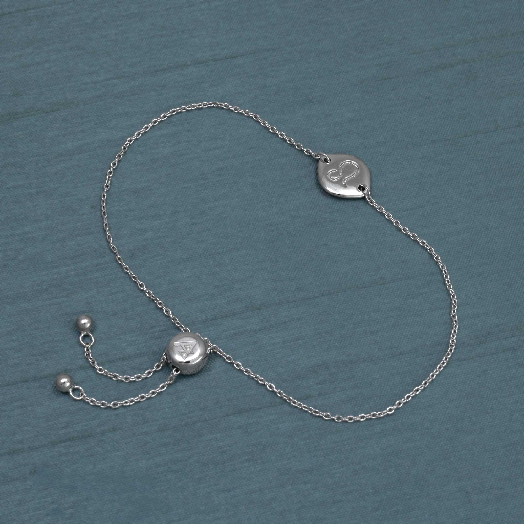 Delicate sterling silver bracelet featuring an adjustable sliding bead and a polished charm engraved with the Leo zodiac symbol, displayed on a muted blue surface.