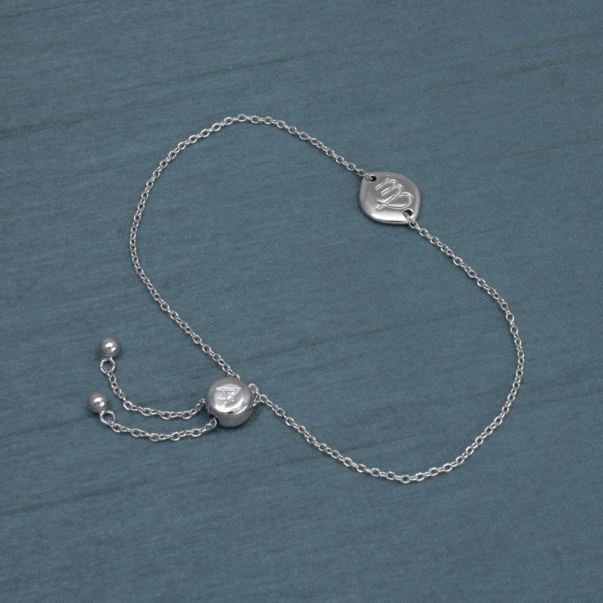 Delicate sterling silver bracelet featuring an adjustable sliding bead and a sculpted Virgo zodiac charm, displayed on a textured blue-grey background.