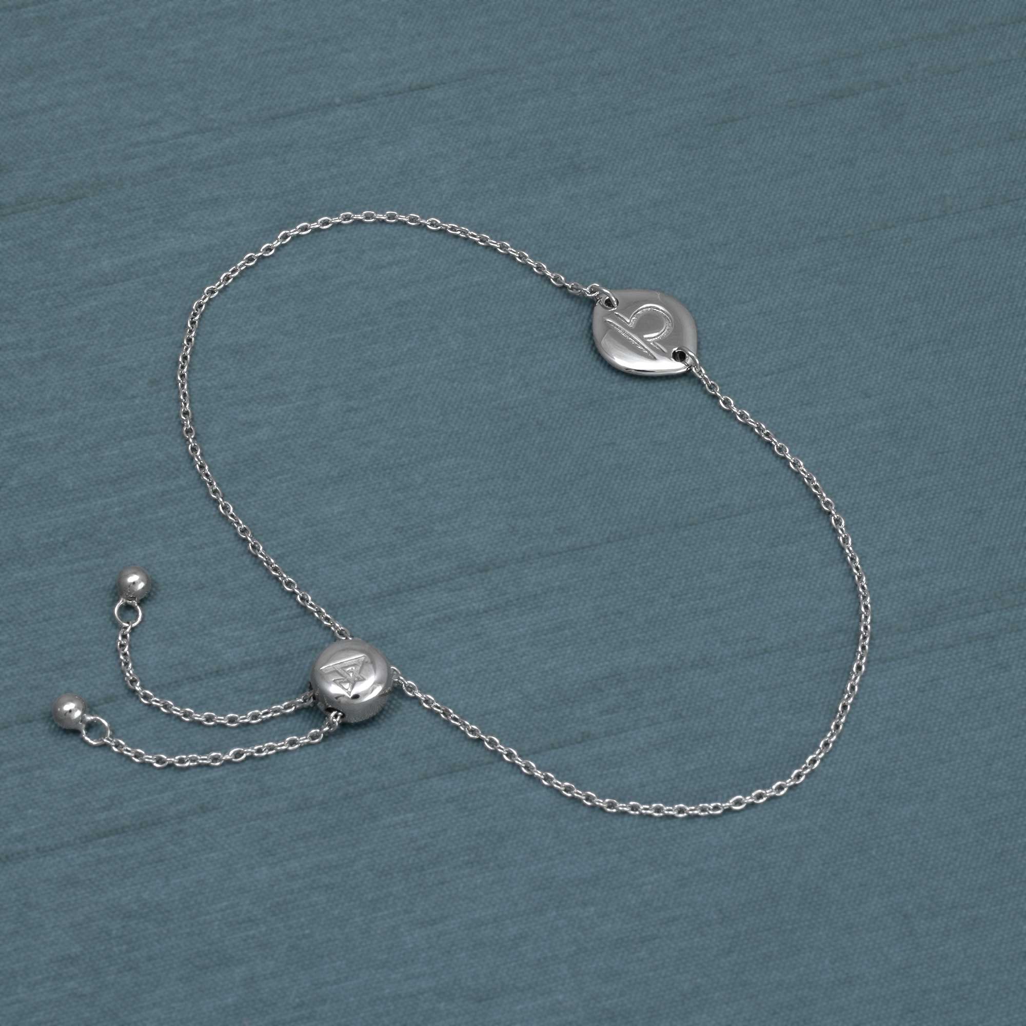 Delicate sterling silver adjustable bracelet featuring a Libra zodiac charm and sliding bead closure, styled on a textured slate blue fabric background.