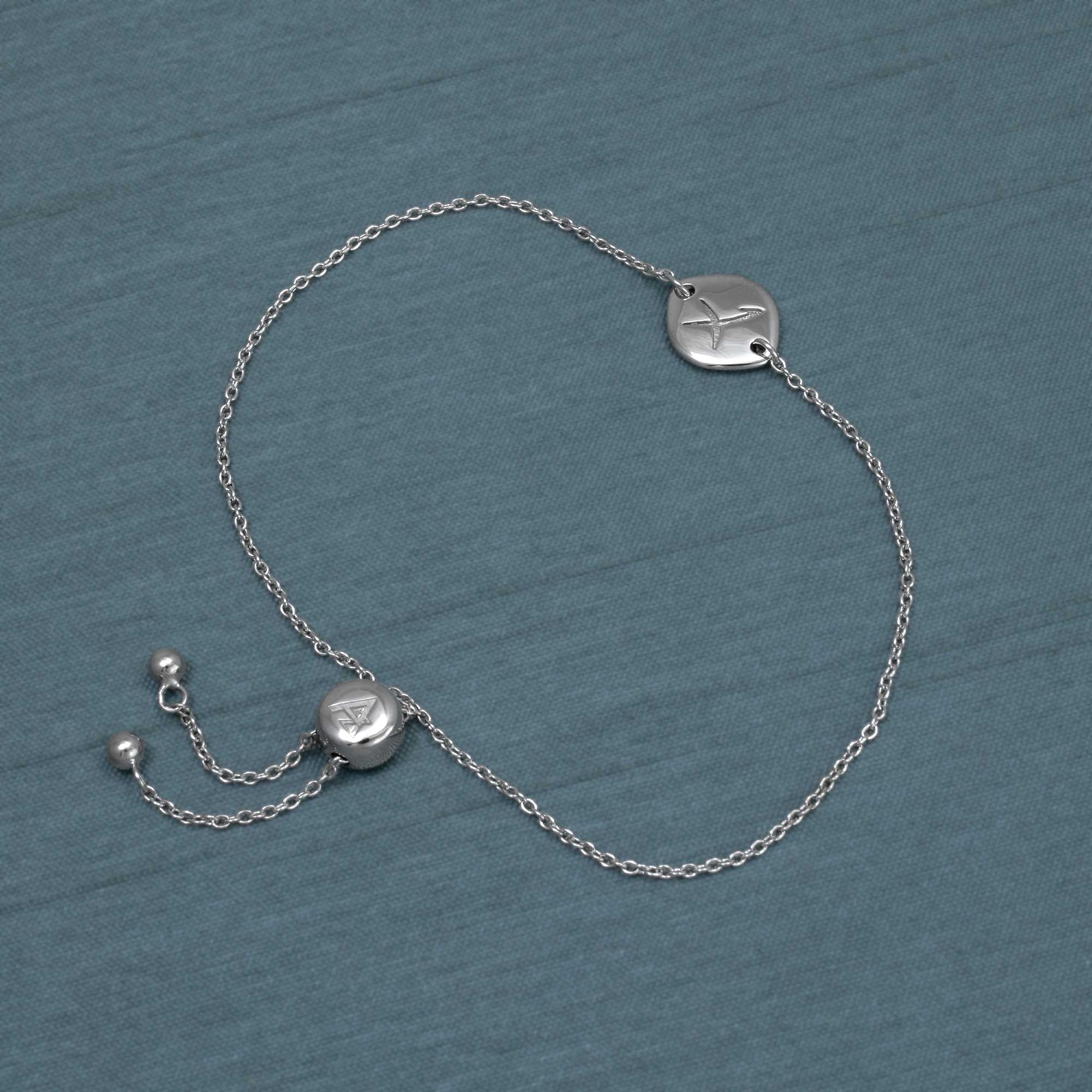 Delicate sterling silver adjustable bracelet featuring a smooth circular charm engraved with the Sagittarius zodiac symbol, displayed on a muted blue background.