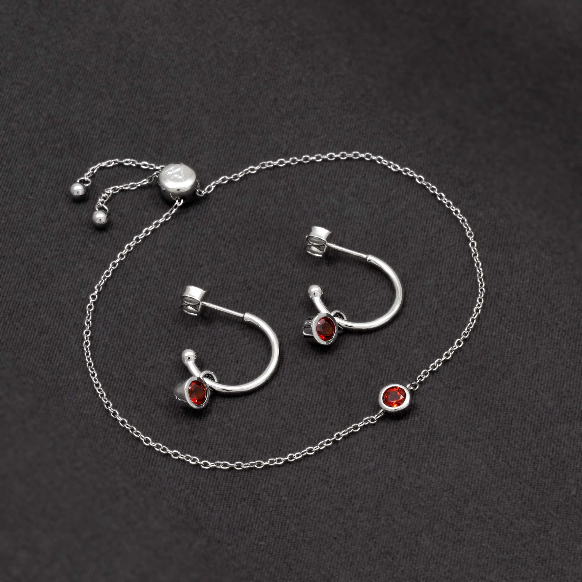 Delicate sterling silver hoop earrings featuring deep red garnet stones, paired with a fine chain bracelet showcasing a matching garnet bezel, embodying refined craftsmanship.