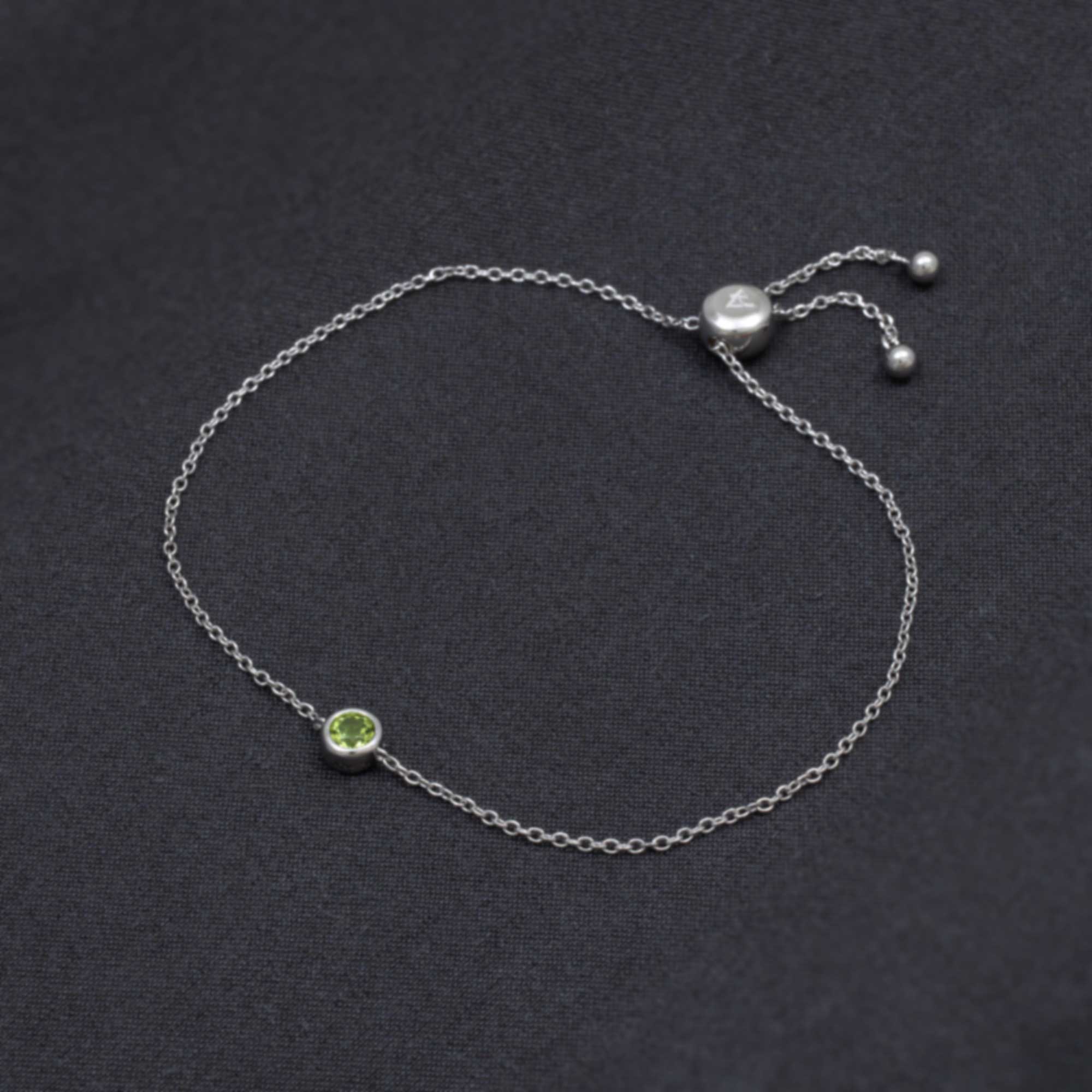 Delicate sterling silver bracelet featuring a bezel-set peridot gemstone and adjustable sliding clasp, embodying refined craftsmanship and a modern, minimalist design.