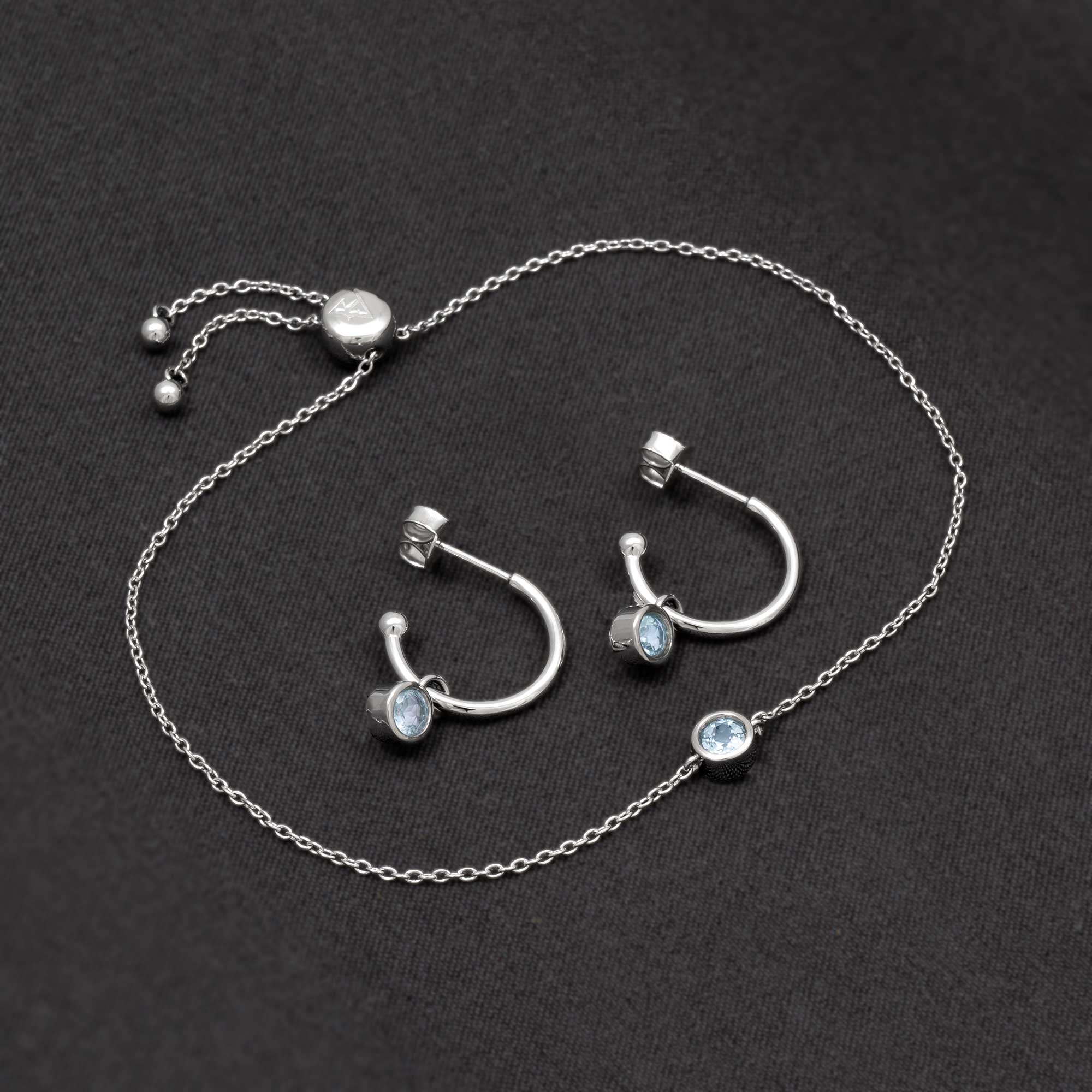 Delicate sterling silver hoops featuring round blue topaz stones with a matching adjustable silver chain, embodying refined craftsmanship and contemporary elegance.