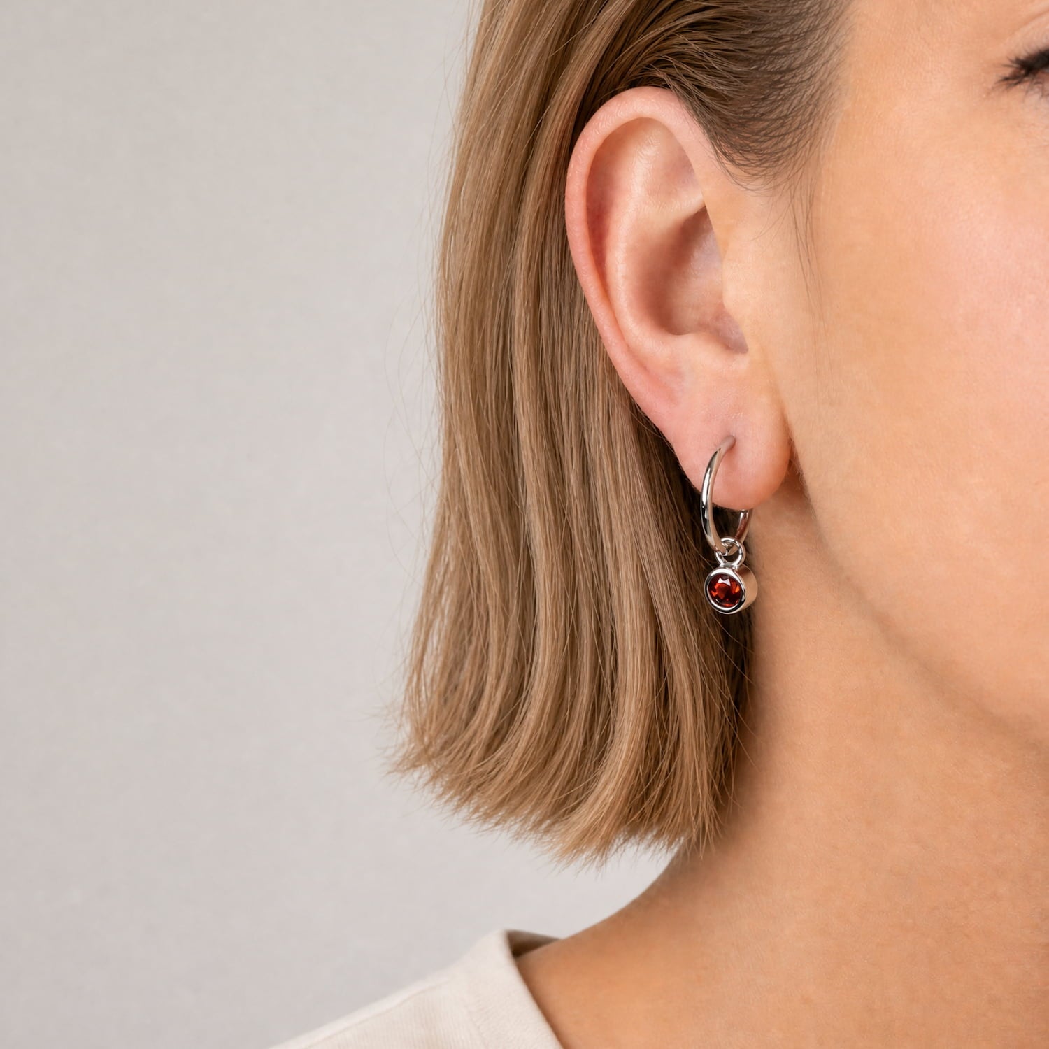 Model wears sterling silver hoop earrings featuring round garnet stones, combining contemporary design with expert British craftsmanship