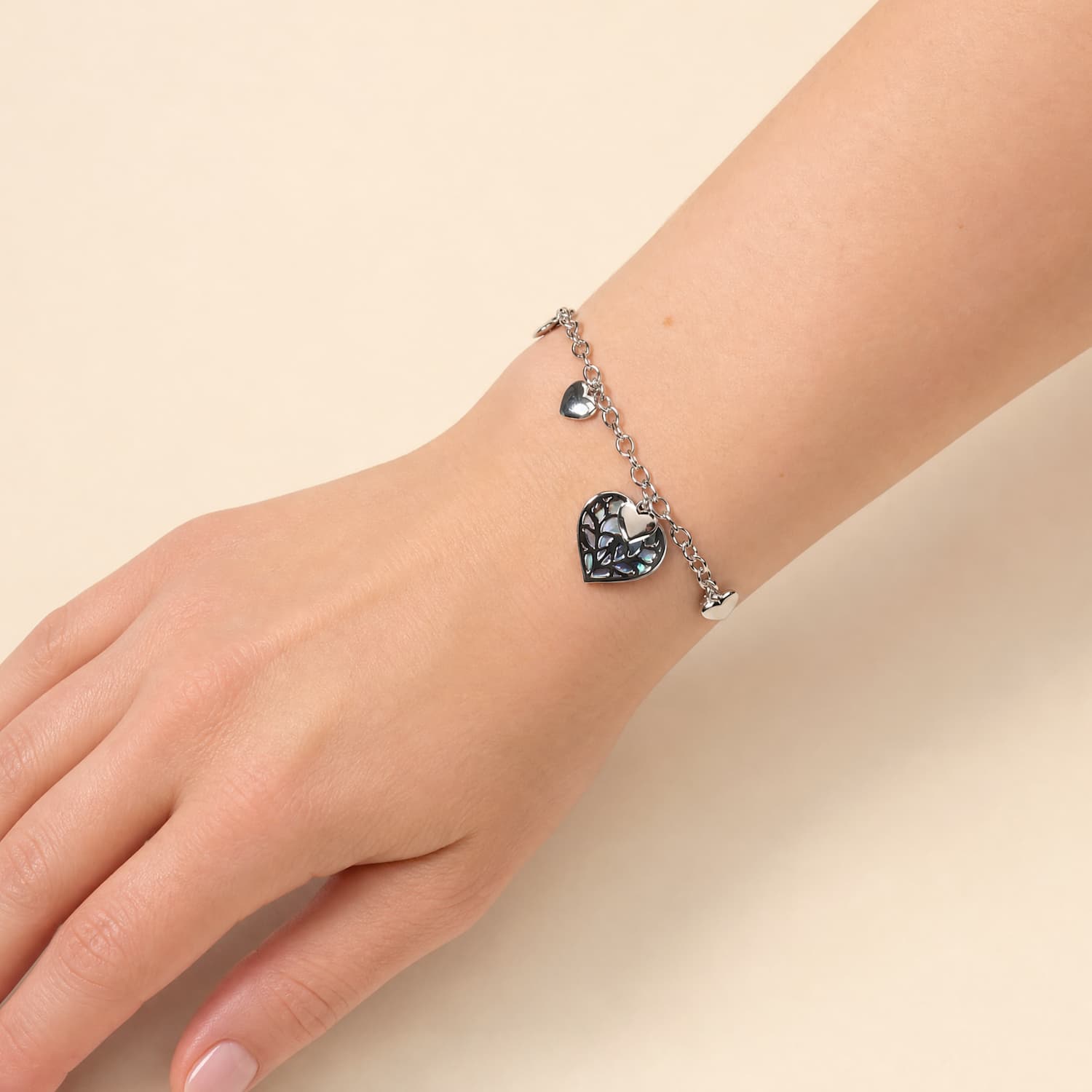 Model wears sterling silver bracelet featuring multiple polished heart charms and a central openwork heart pendant with abalone inlay.