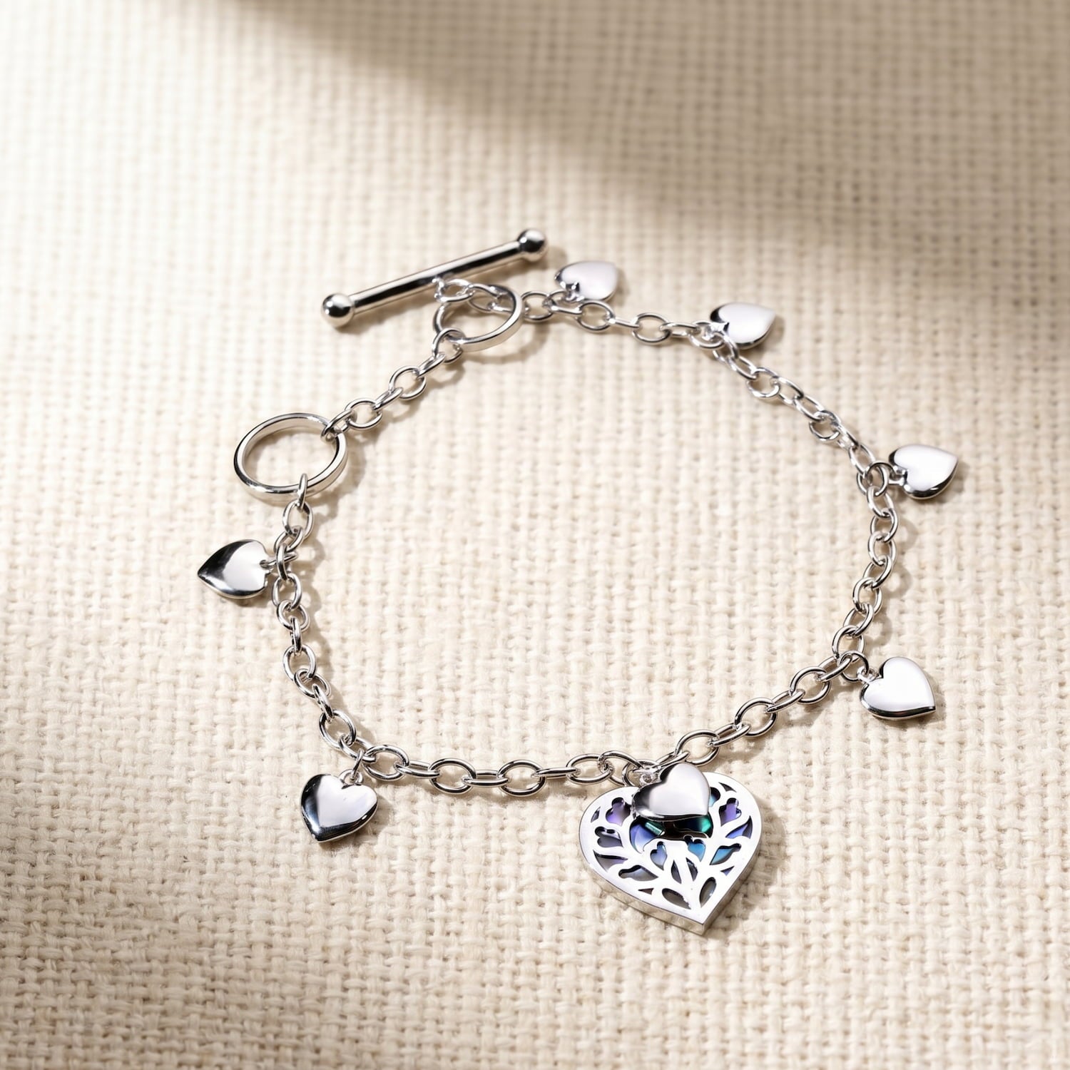 Sterling silver bracelet featuring multiple polished heart charms and a central openwork heart pendant with abalone inlay, secured by a T-bar clasp.