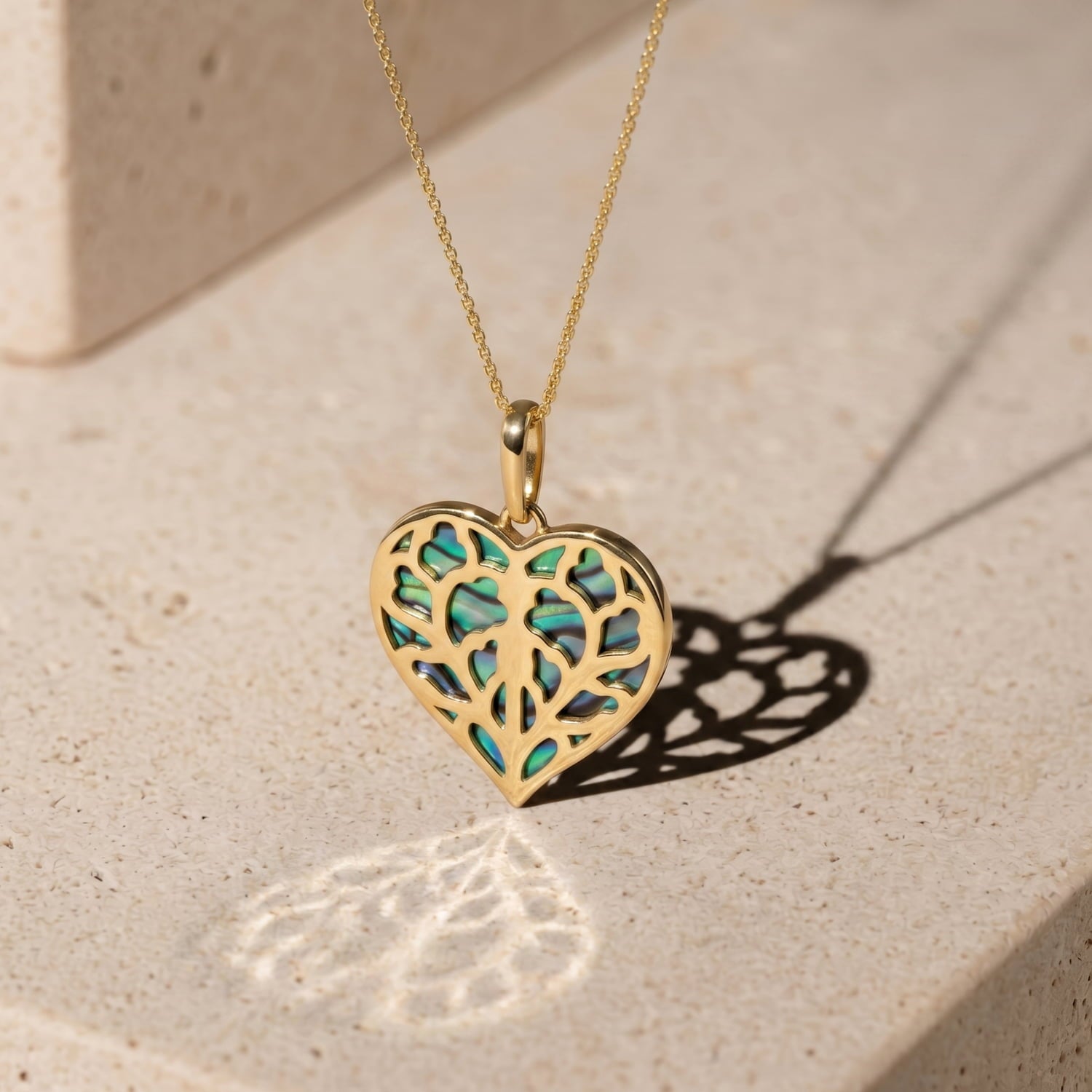 9 carat yellow gold pendant in a heart shape featuring intricate openwork with iridescent abalone inlay against a polished limestone background