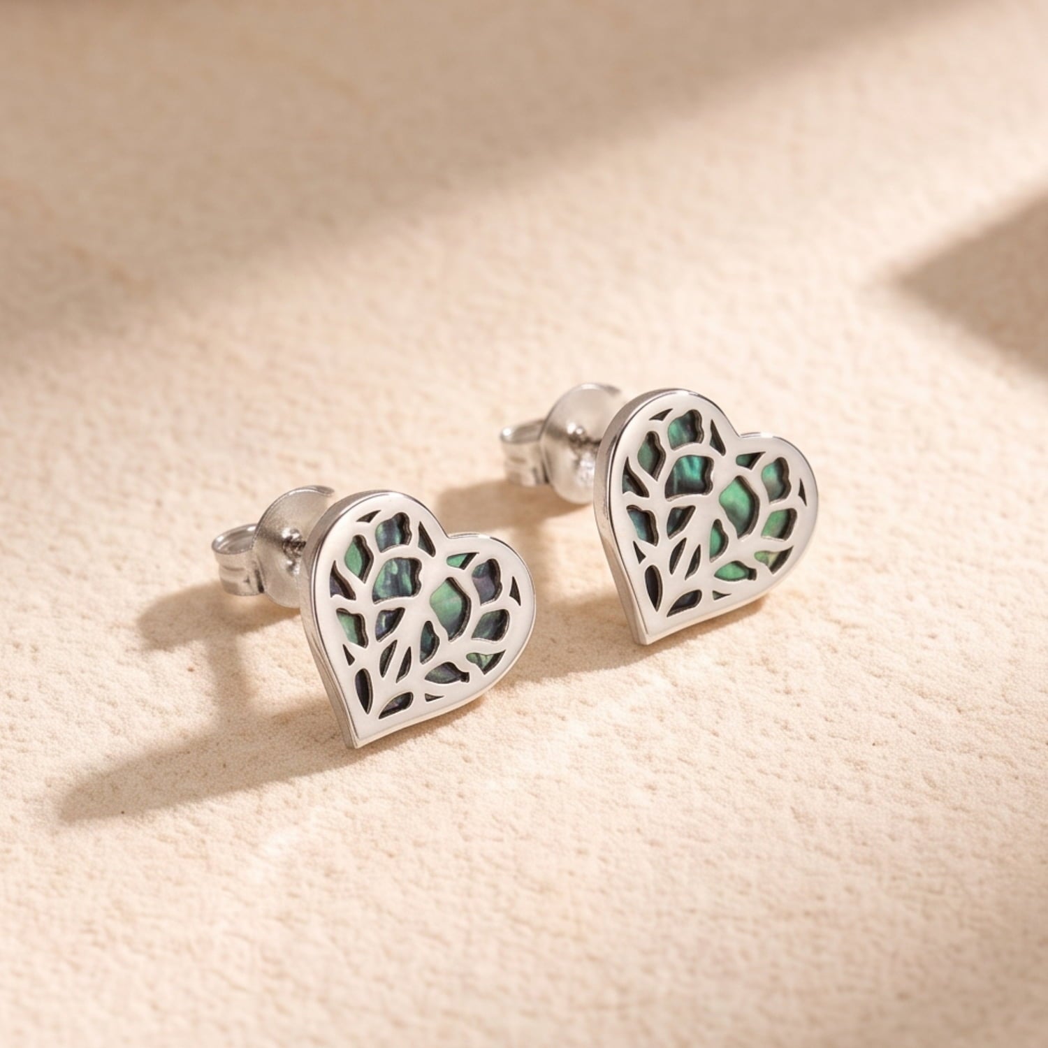 Pair of 9 carat white gold stud earrings featuring heart-shaped openwork design with iridescent abalone inlay, combining sculptural elegance with a contemporary finish.