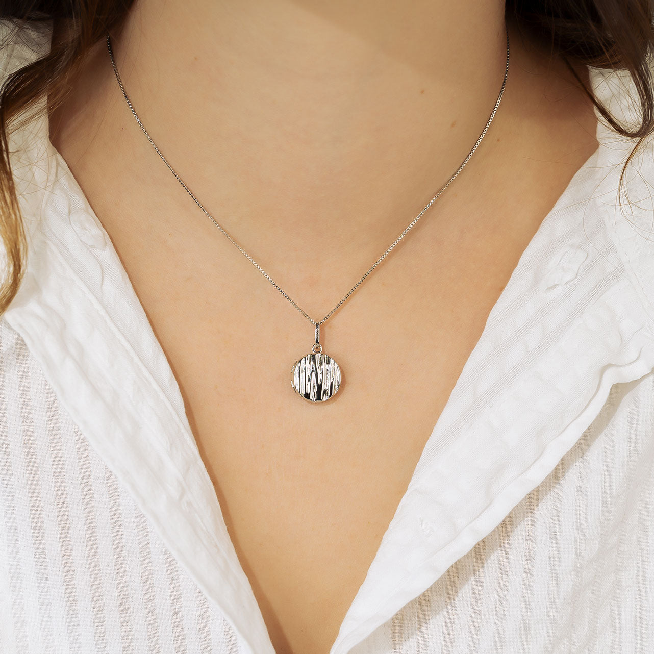 Sterling silver pendant with a grooved textured surface on a slender adjustable chain, styled against a white shirt collar for a refined and sculptural look.