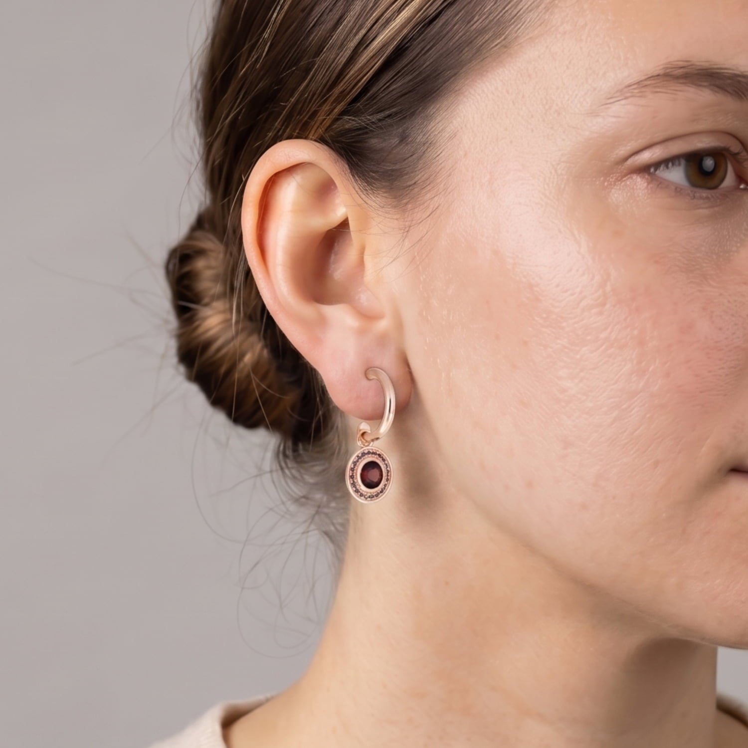 Model wears a pair of rose gold vermeil hoop earrings featuring oval garnet and amethyst gemstones set within decorative bezels, showcasing an elegant and sculptural design.