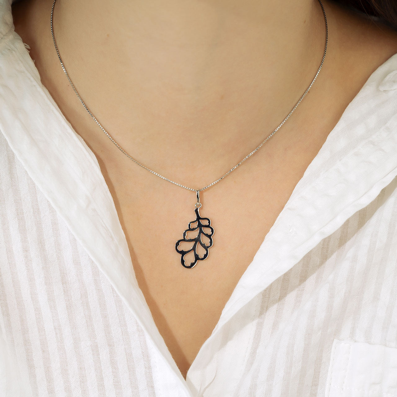 Delicate sterling silver necklace featuring a sculptural oak leaf pendant with openwork design, styled with a crisp white shirt for an elegant yet natural look.