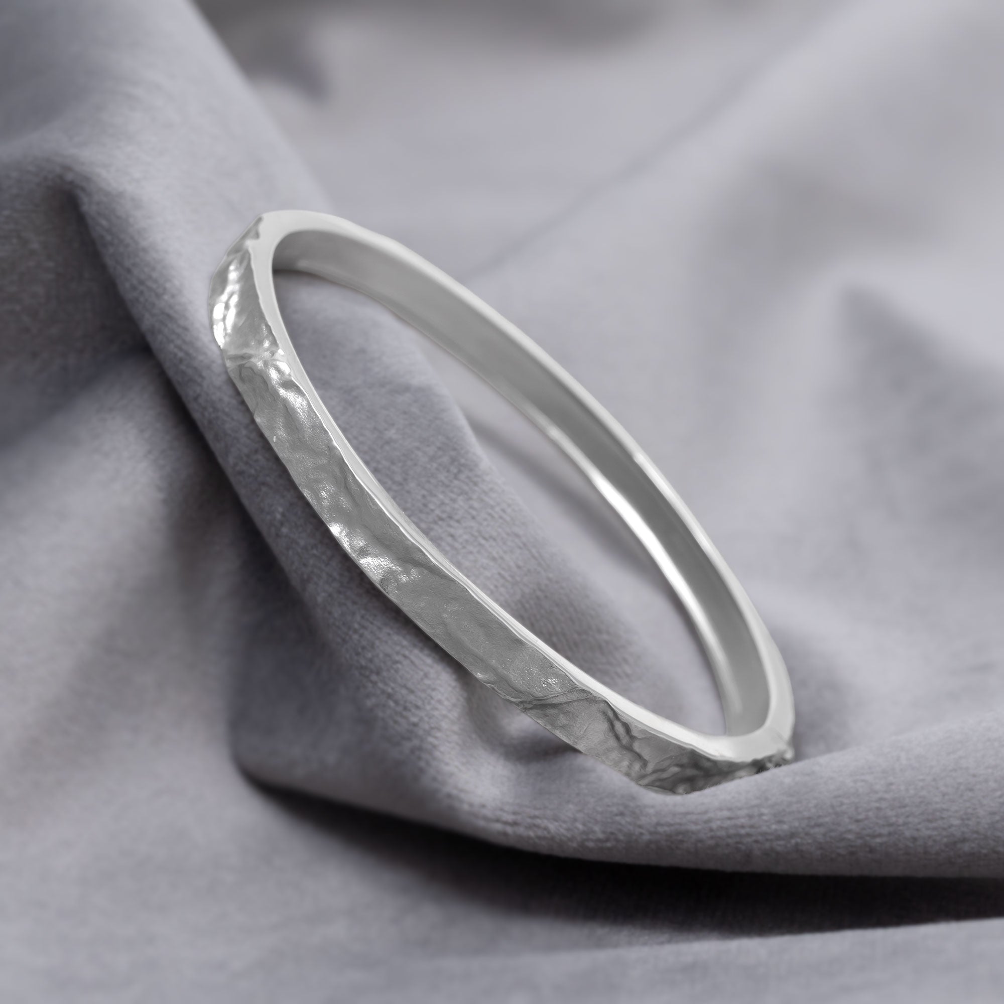 Sterling silver bangle featuring a sculpted textured band with a polished interior and secure clasp, showcasing contemporary British silver jewellery craftsmanship by Azendi. Placed on a grey velvet cloth.