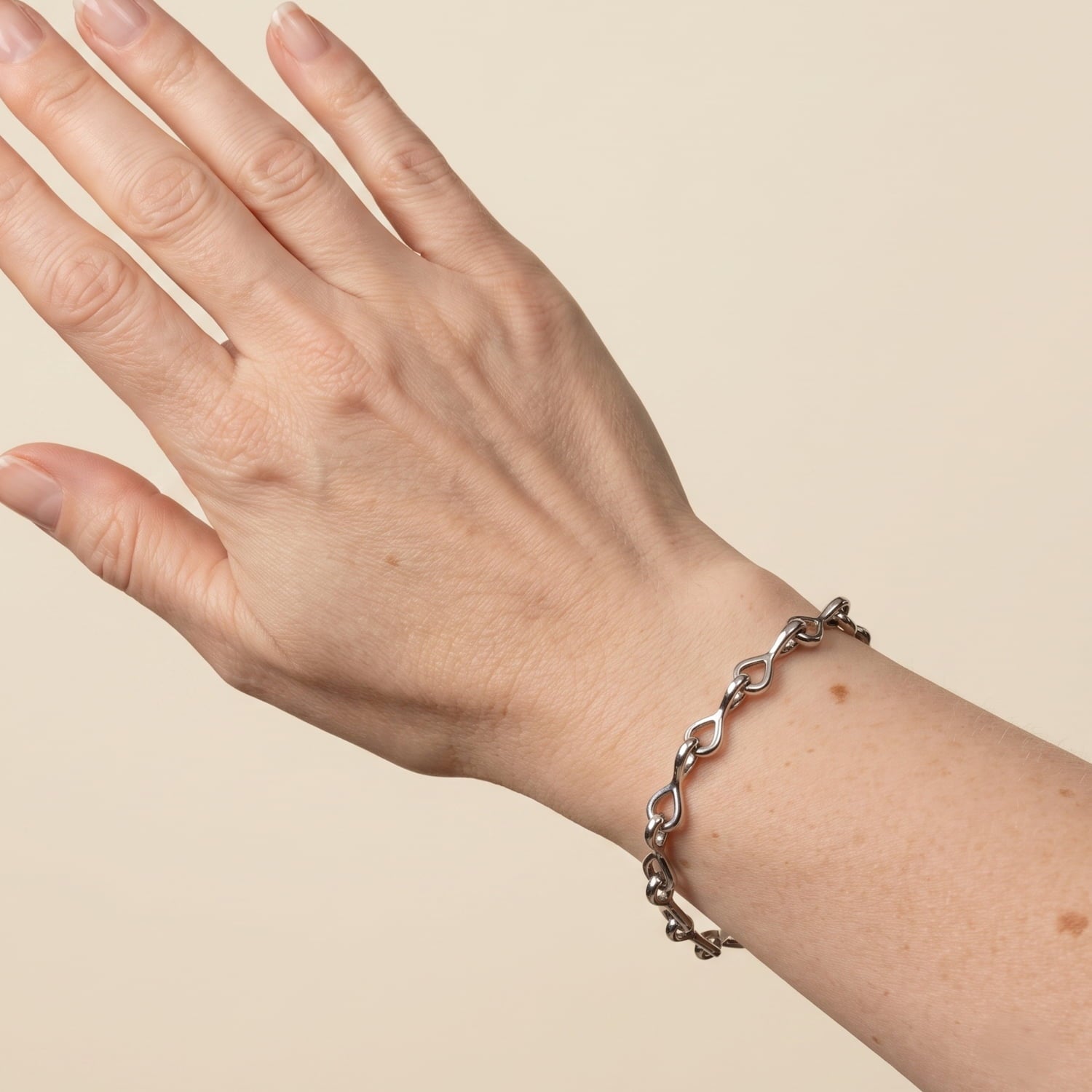 A close-up of a person's hand and wrist wearing a sterling silver link bracelet against a solid beige background.