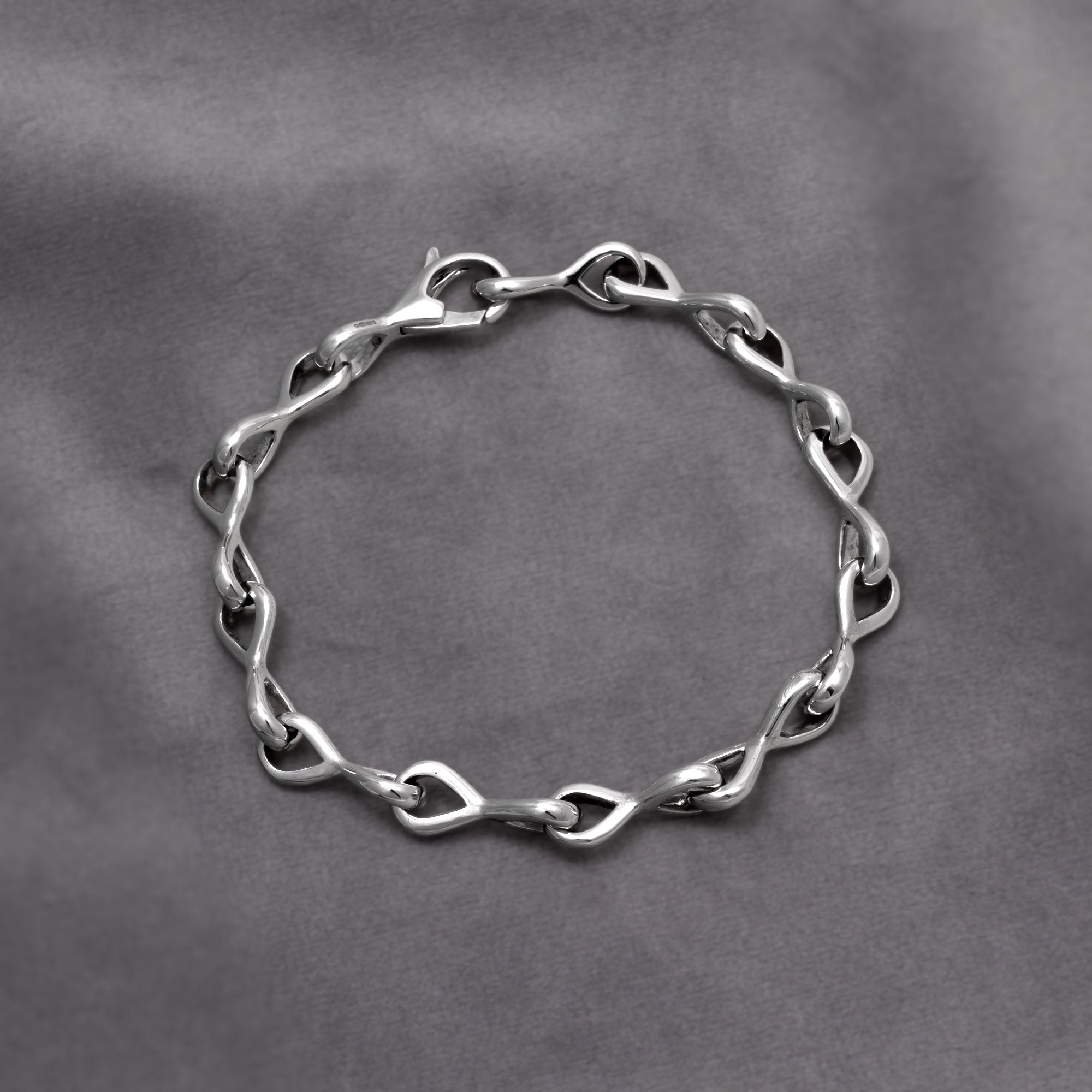 Bracelet featuring interlocking teardrop links with smooth, flowing contours for a modern, sculptural expression in silver jewellery. Placed on a grey velvet cloth.