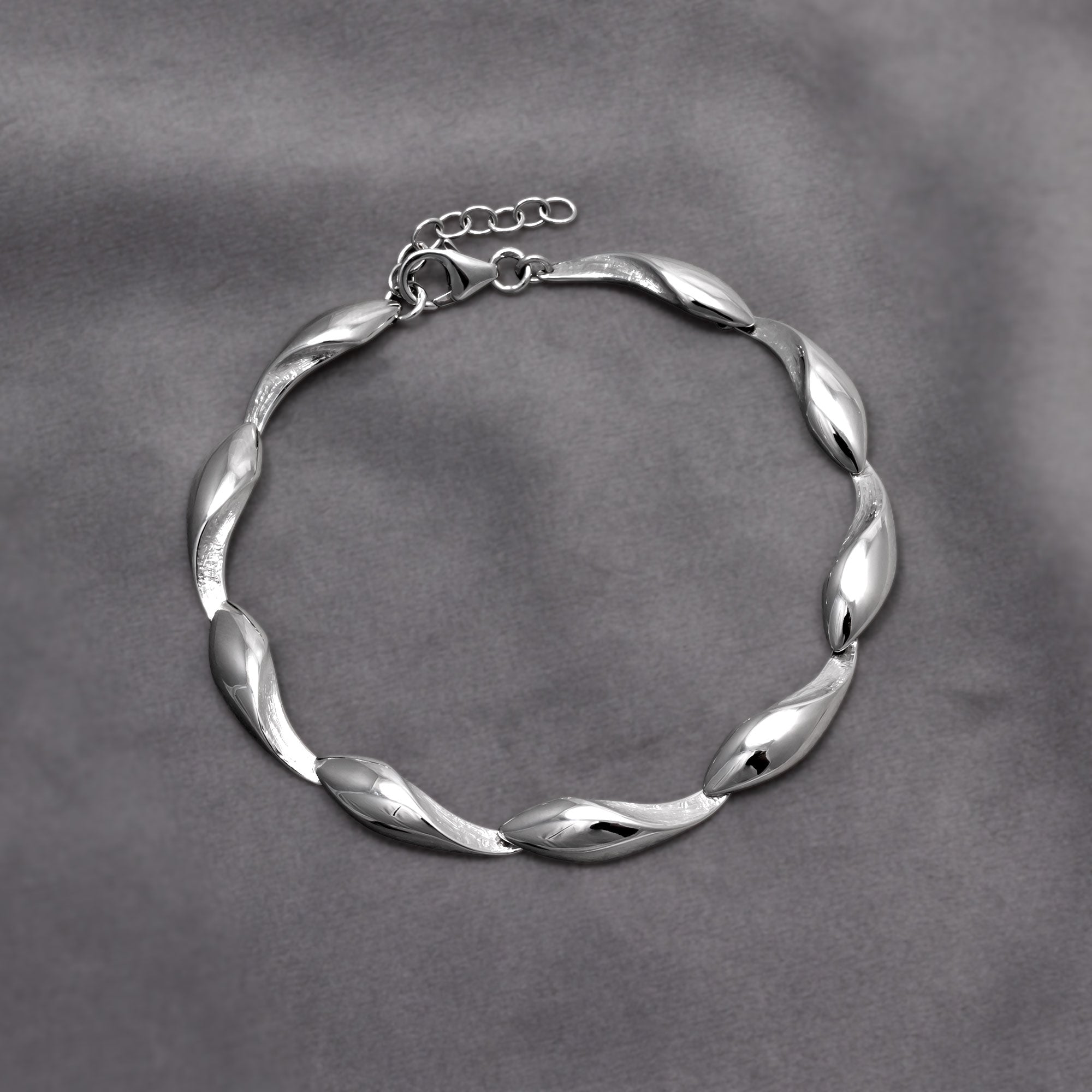 Sterling silver jewellery featuring a sculptural twisted wave motif, the bracelet has a polished and textured finish. Placed on a grey velvet cloth.