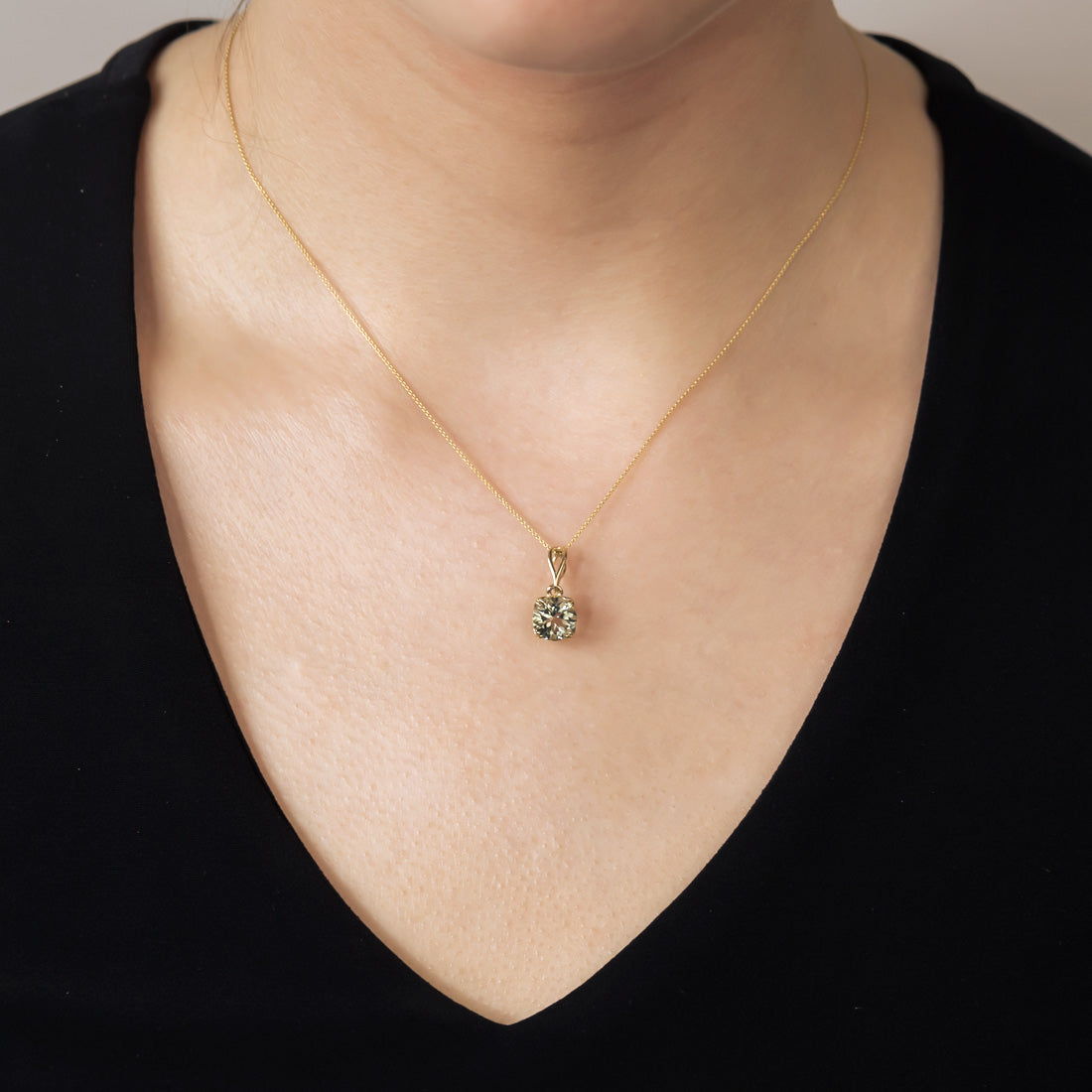 A slender 9 carat gold necklace featuring a green amethyst solitaire pendant, highlighting a refined and elegant design worn against a black top.