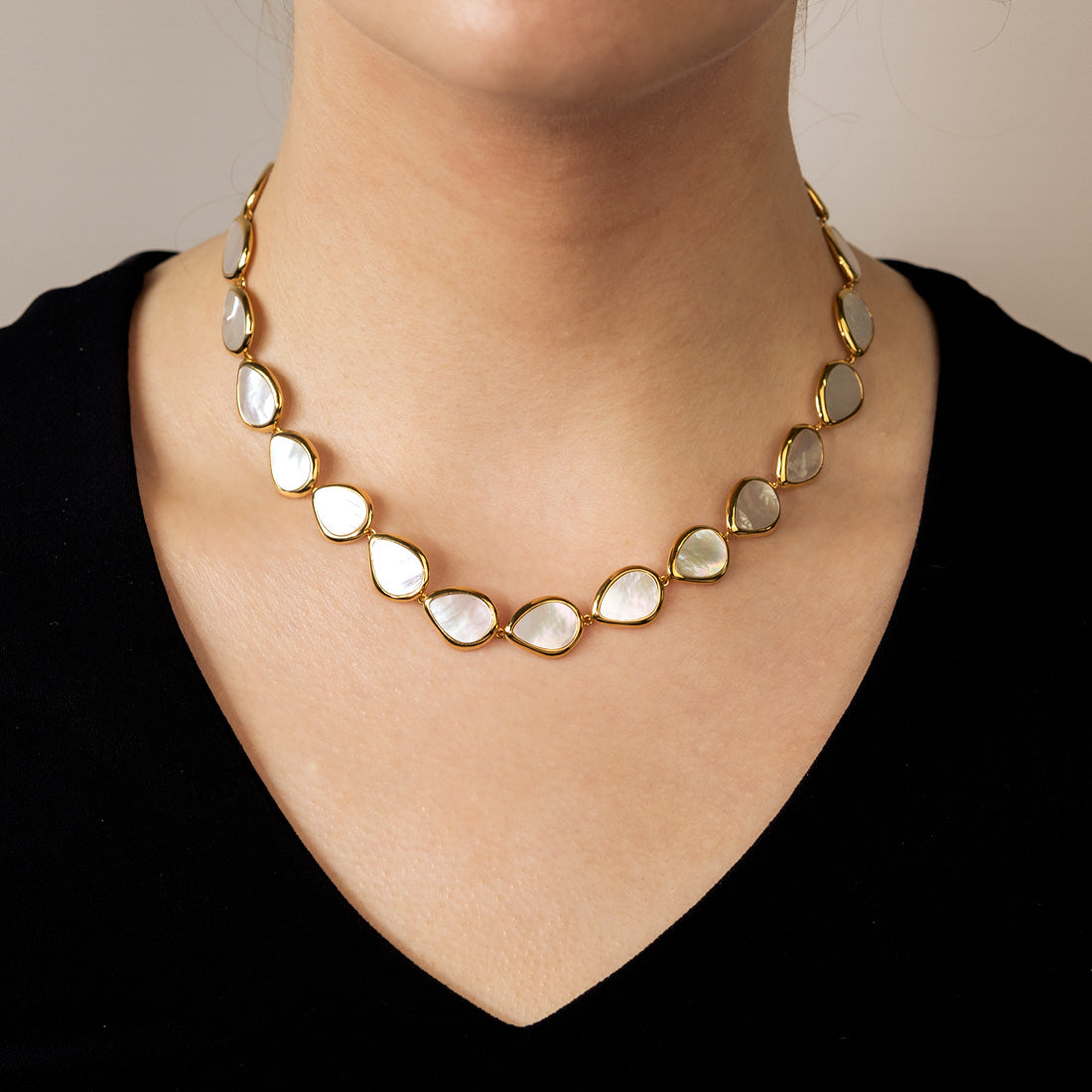 Necklace featuring linked gold vermeil frames each holding an irregular mother of pearl element, worn against a simple black top for an elegant statement look.