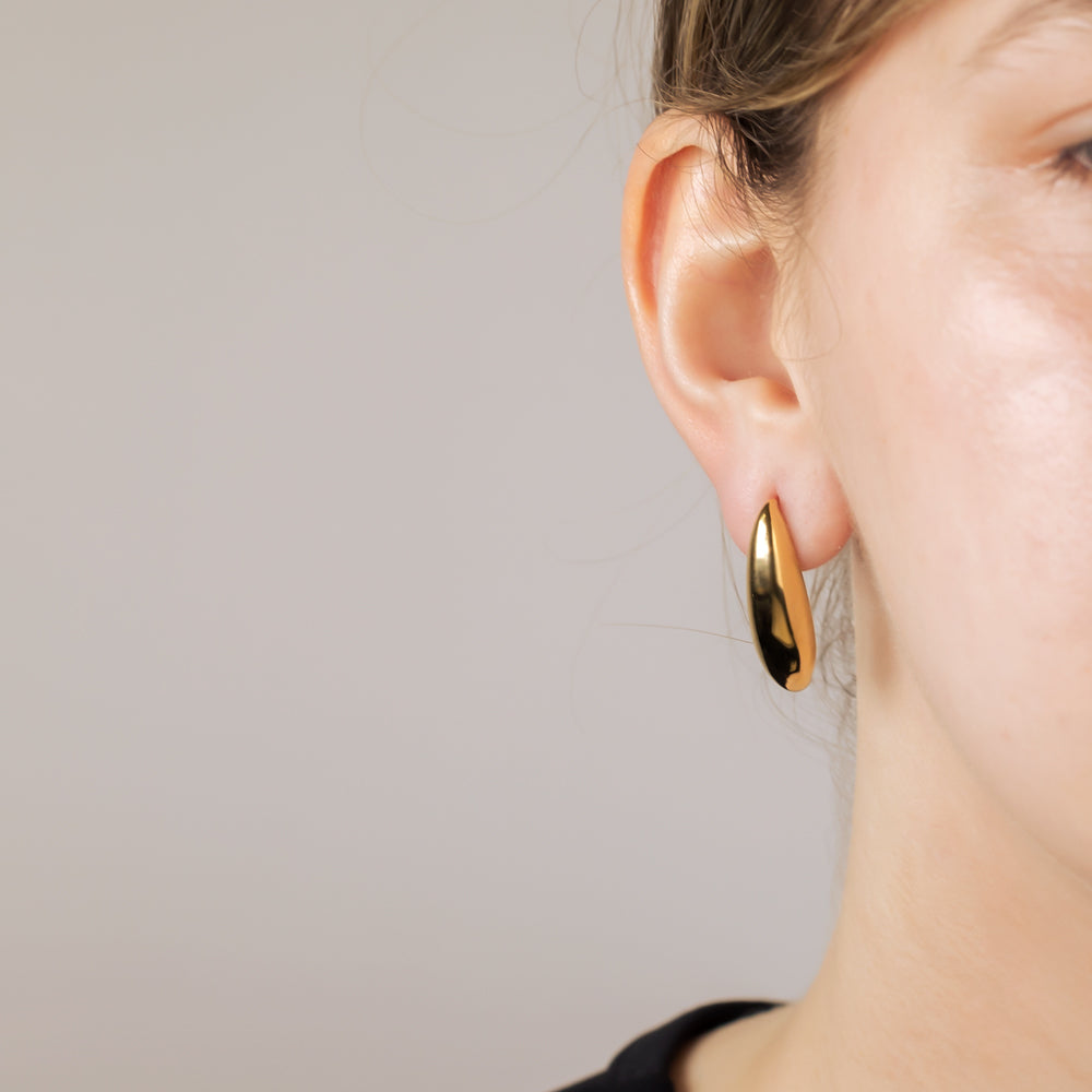 Close-up of an ear adorned with a single large gold vermeil earring featuring a smooth, elongated curved design, highlighting elegant contemporary silver jewellery by Azendi.